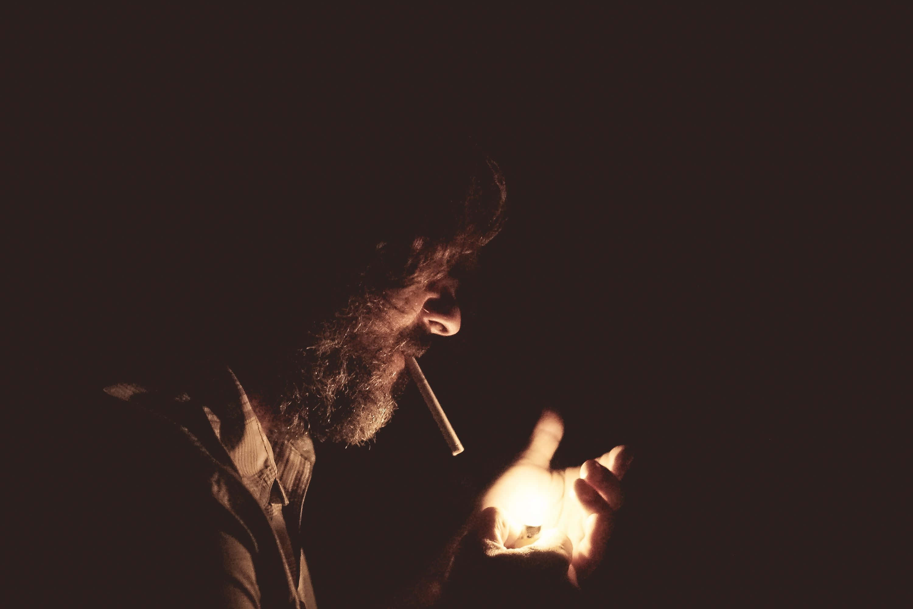 Soulful 桌布 壁紙 — 一個留鬍子的男人在黑暗中拿著一個發光的物體，同時在陰鬱的低光場景中抽煙。