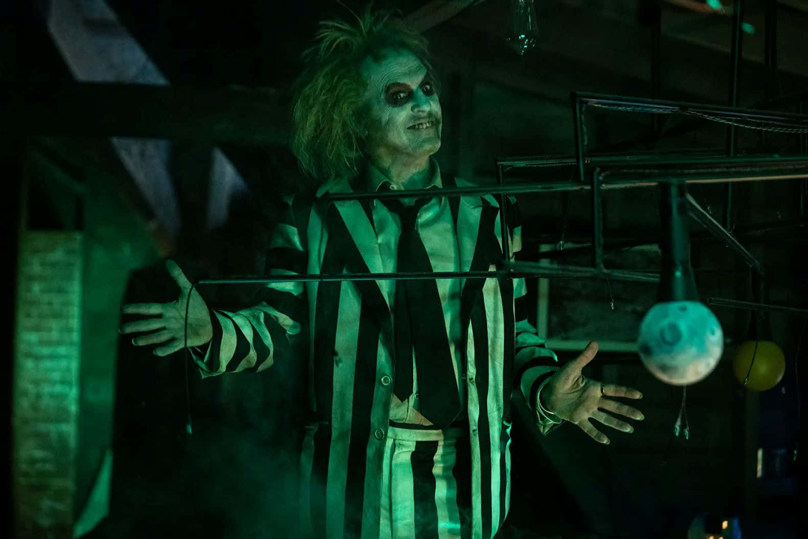  壁紙 — Beetlejuice 站在一個昏暗的綠色房間裡，張開雙臂，露出頑皮的笑容。