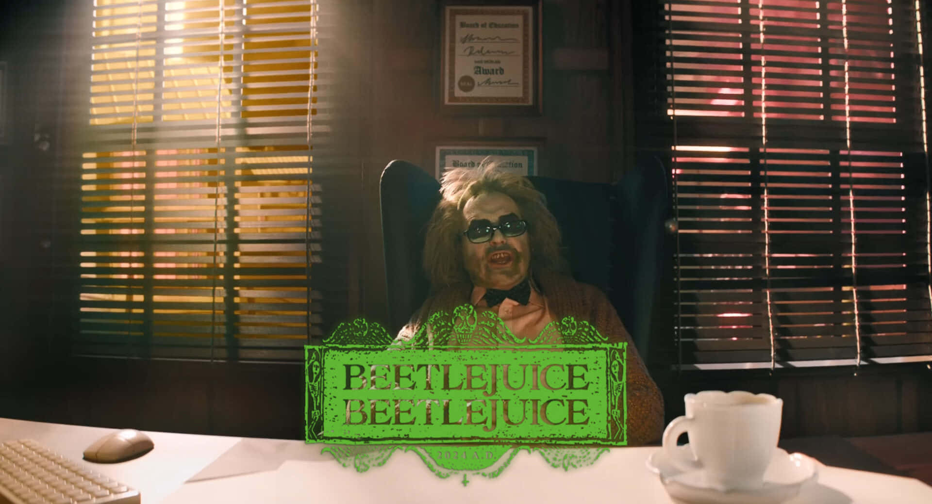  壁紙 — Beetlejuice 坐在昏暗的辦公椅上，身後是帶有百葉窗投射光線條紋的辦公桌，旁邊有一個發光的綠色標題卡和一杯咖啡。