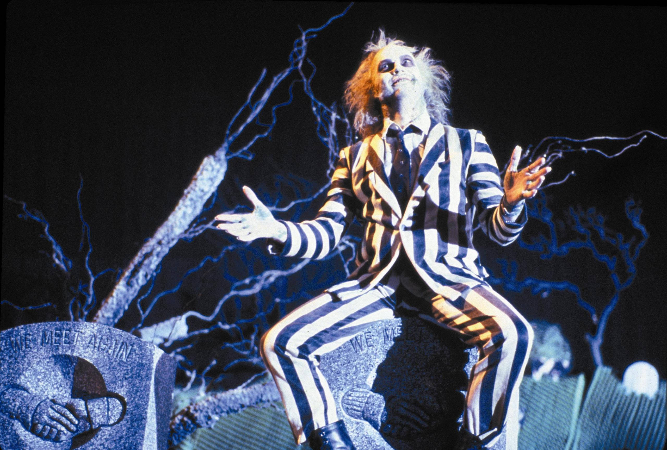 Beetlejuice 桌布 壁紙 — Beetlejuice 穿著標誌性的條紋西裝坐在墓碑上，周圍閃電劈啪作響，背景漆黑。