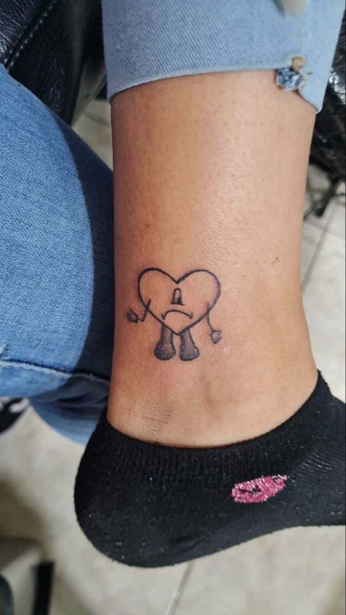 Bad Bunny Heart 桌布 壁紙 — 一個細小的黑色墨水刺青，圖案是一個悲傷的卡通心形，有手有腳，位於一個人的腳踝上。