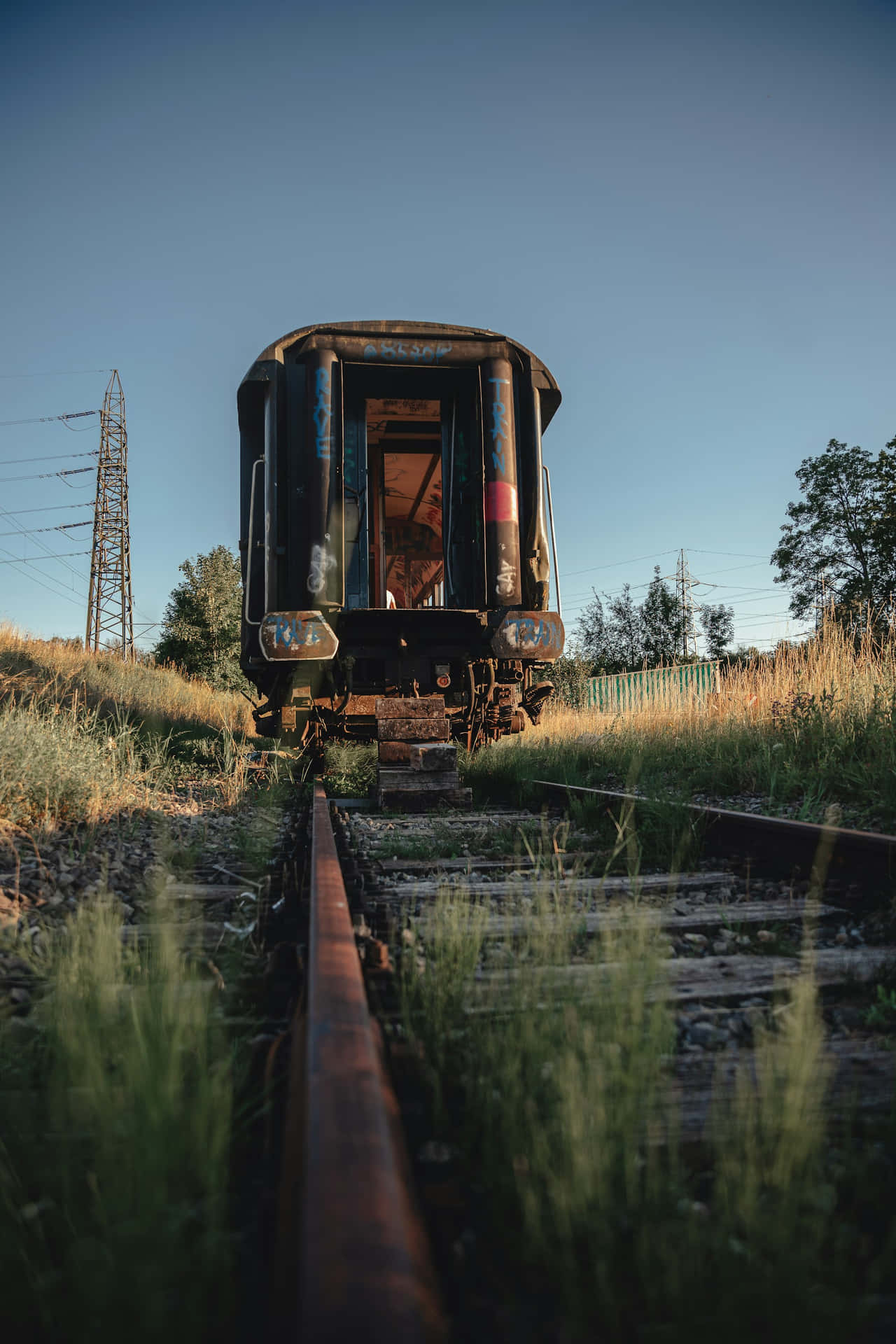  壁紙 — 一輛被遺棄的火車車廂生鏽且被遺忘在雜草叢生的軌道上，在黃金時段清澈的藍天下。