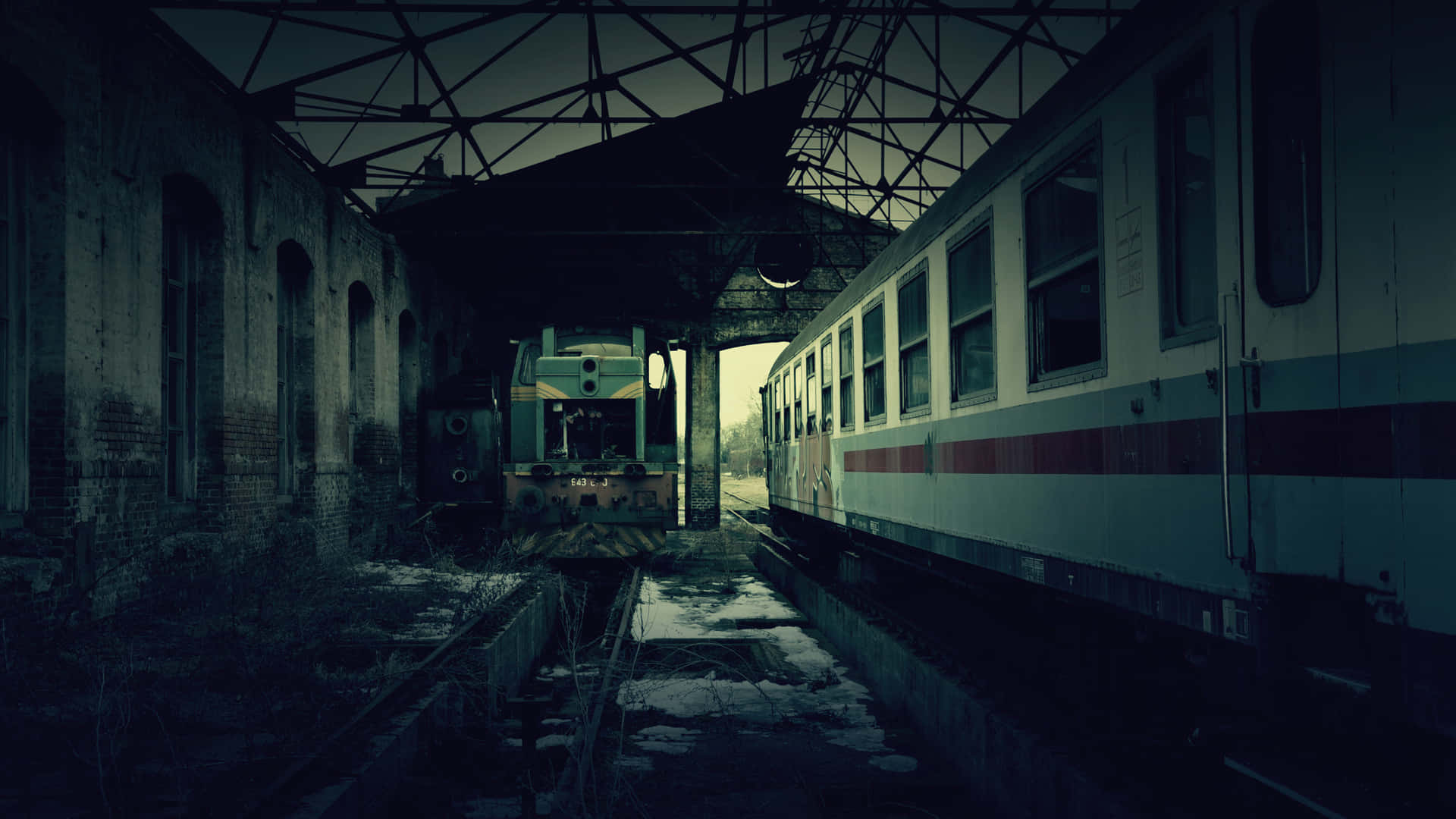  壁紙 — 被遺棄的火車在破舊的車站屋頂下靜止不動，微弱的暮色中雪花灑落在鐵軌上。