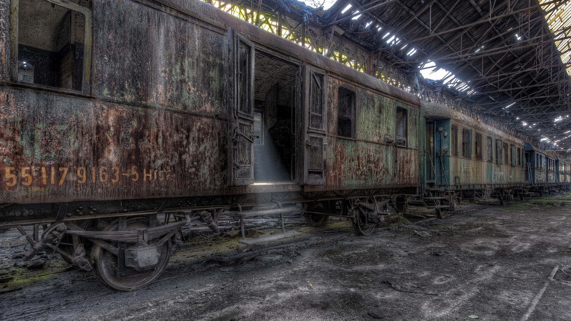  壁紙 — 被遺棄的鏽蝕火車車廂停放在破損屋頂下光線穿透的破舊火車站內。