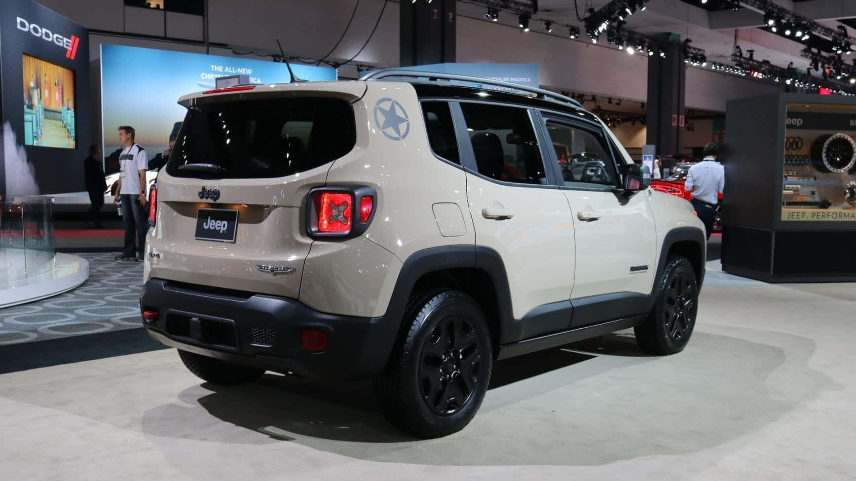 Jeep Renegade 桌布 壁紙 — 一輛米色Jeep Renegade，帶有黑色飾邊和星星貼紙，在明亮的展覽燈光下於車展中展示。