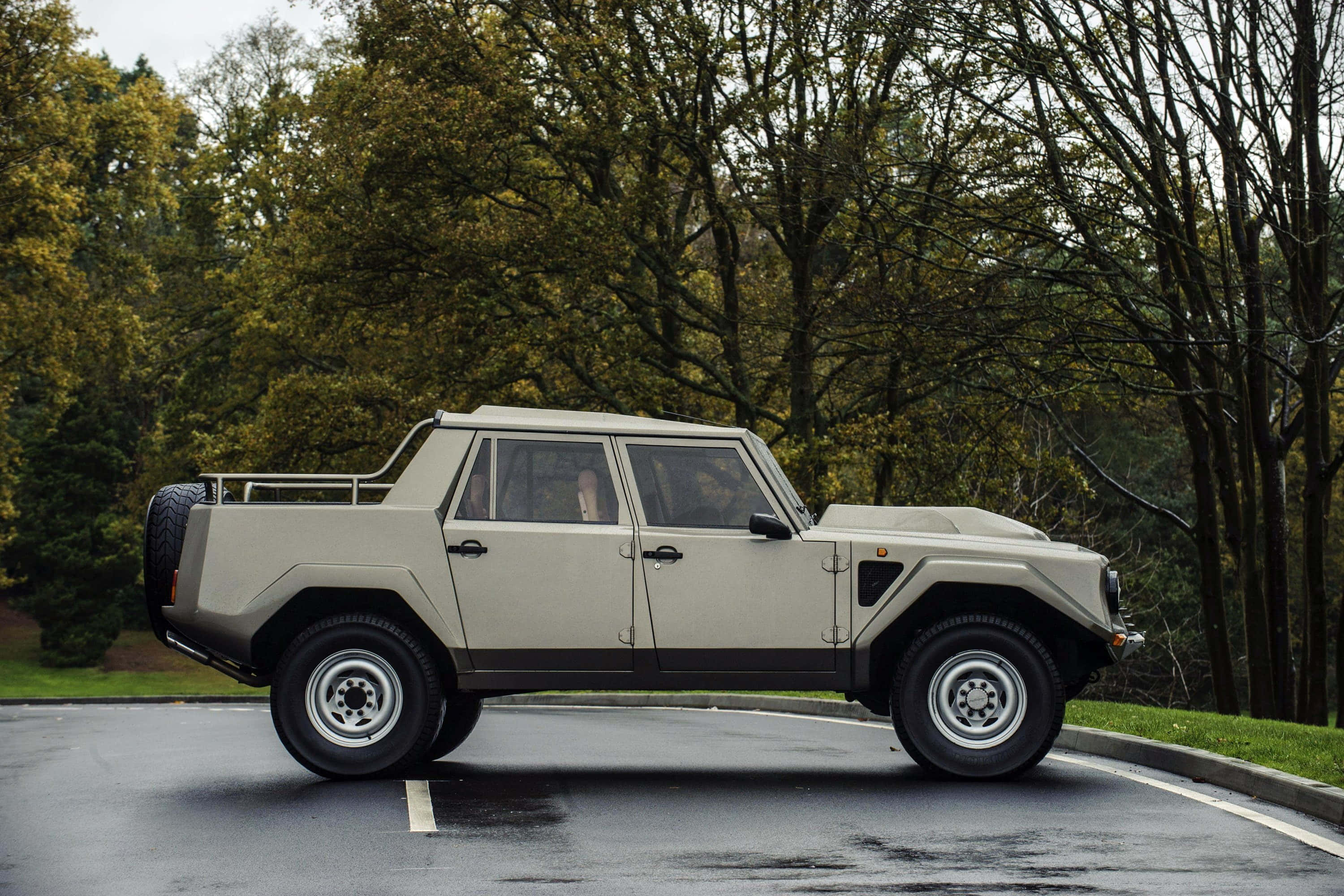 Lamborghini Lm002 桌布 壁紙 — 一輛米色藍寶堅尼LM002 SUV停放在潮濕的柏油路上，周圍環繞著秋天的樹木。