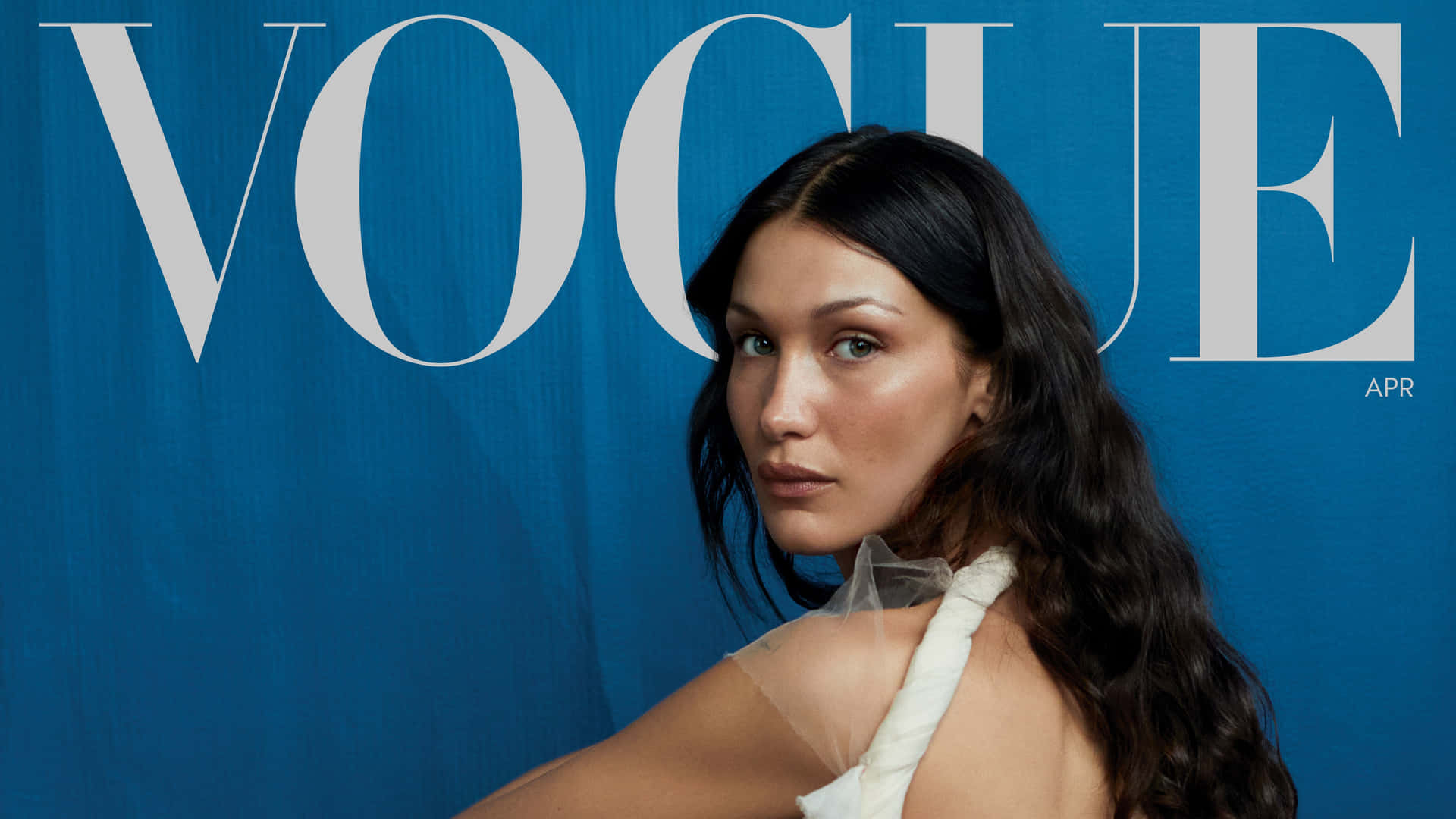 壁紙 — Bella Hadid 自信地穿著白色連衣裙，以大膽的藍色 Vogue 雜誌背景擺姿勢。