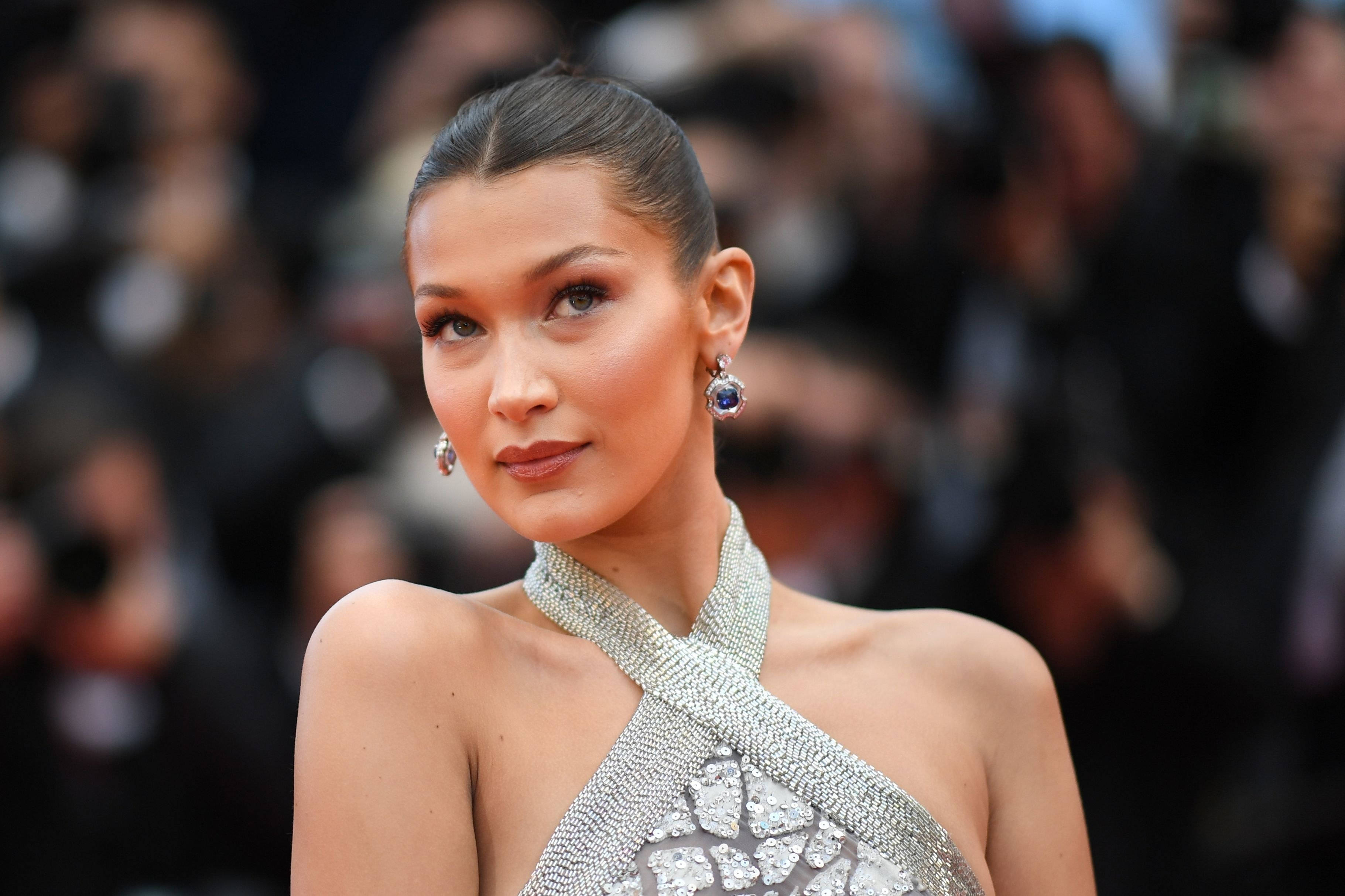Bella Hadid 桌布 壁紙 — Bella Hadid 身穿閃亮銀色禮服，在華麗的紅毯活動中閃耀，身後有模糊的攝影師。