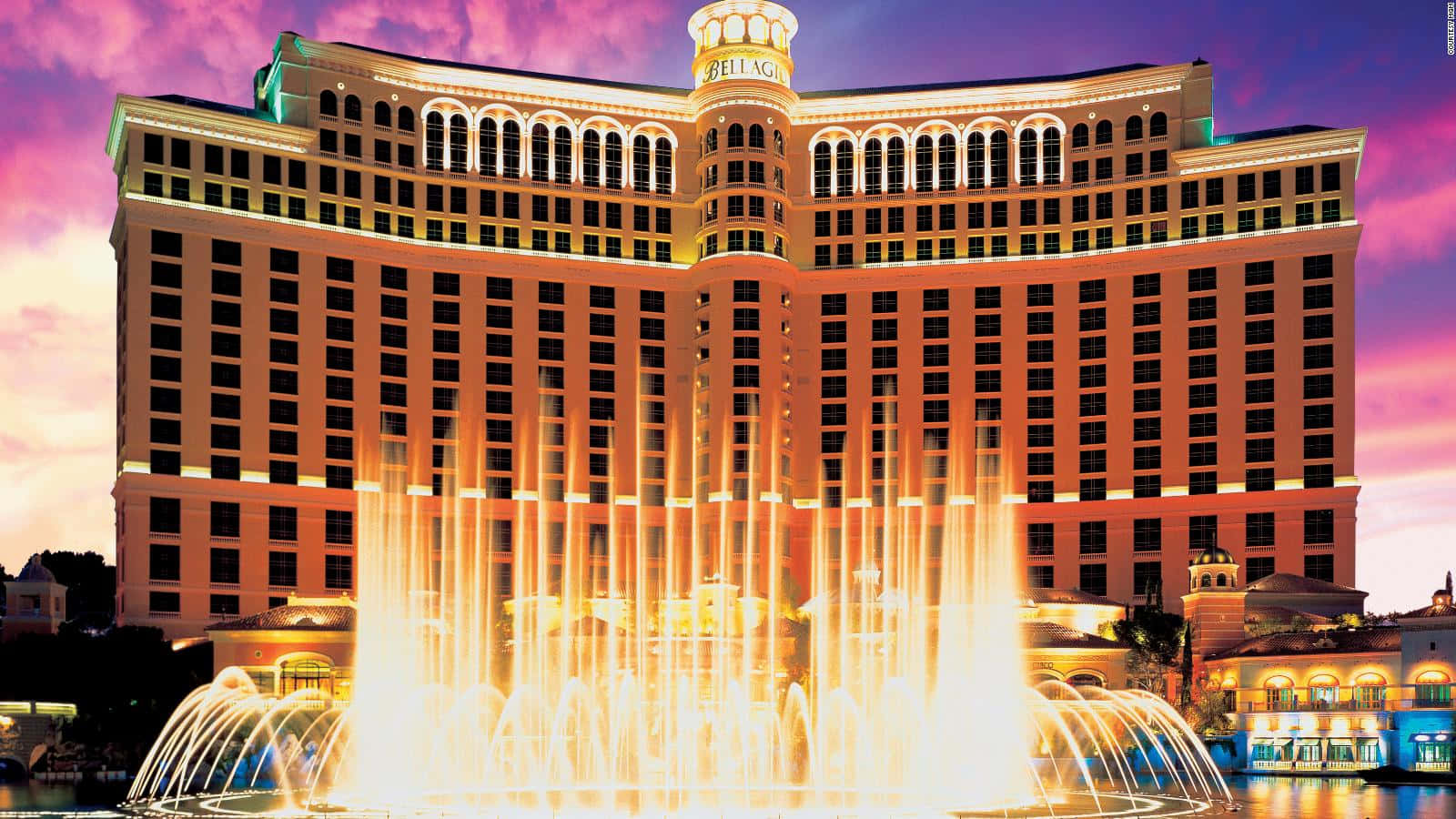 拉斯維加斯 桌布 壁紙 — Bellagio 酒店在粉紅和紫色的暮色天空中溫暖地發光，其標誌性噴泉在前方噴出金色的水。