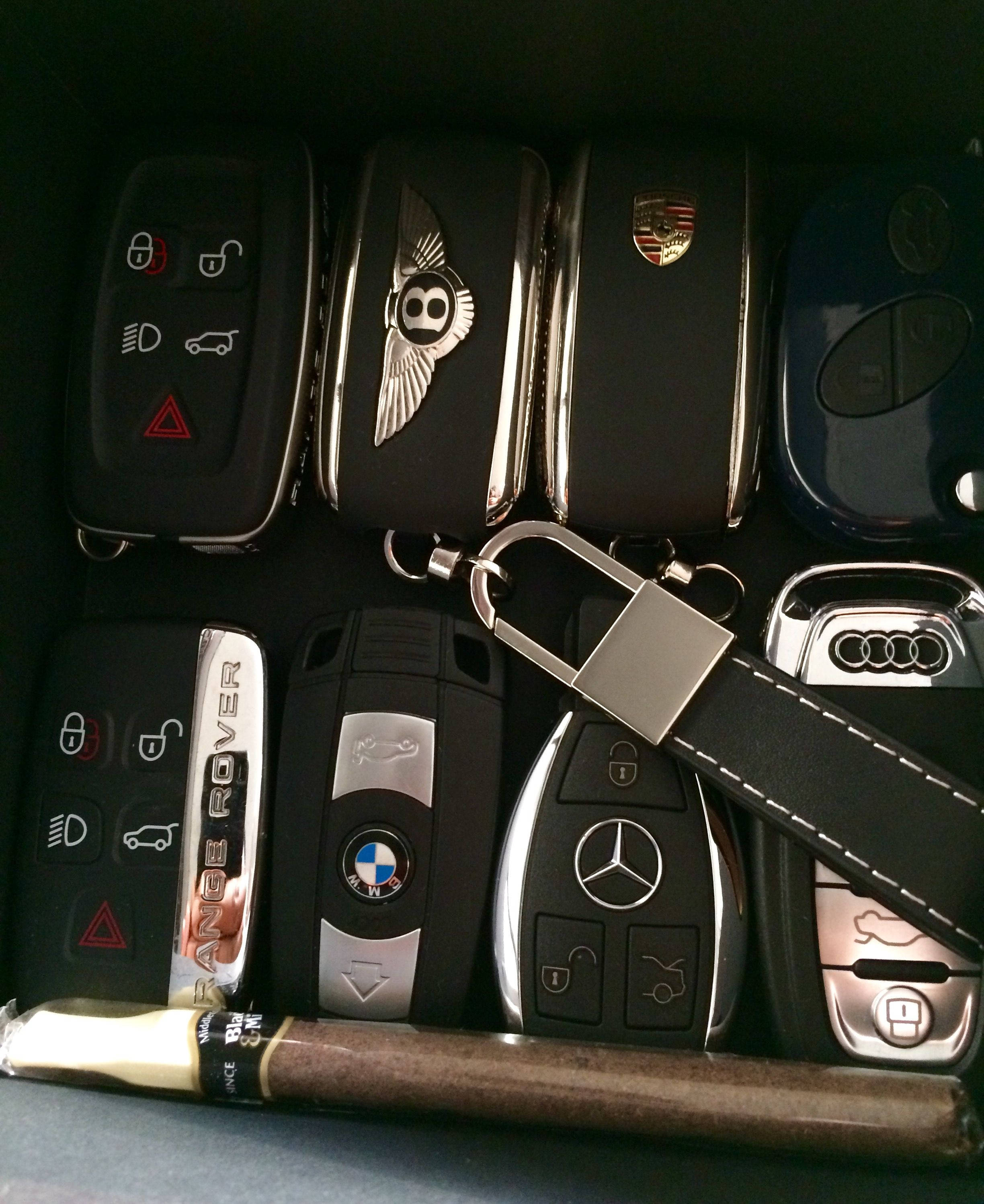 BMW 動圖 桌布 壁紙 — Bentley Range Rover BMW Mercedes 和 Audi 的豪華車鑰匙扣整齊排列，下方放著一支雪茄。