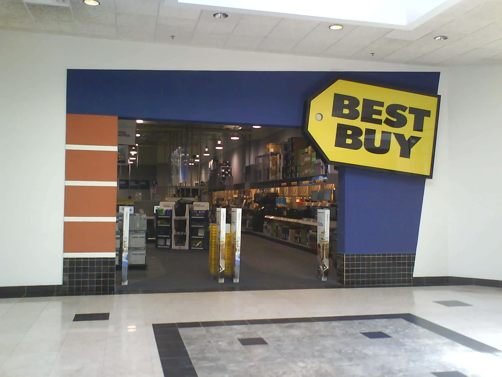 Best Buy 桌布 壁紙 — Best Buy 商店入口，玻璃門上方有一個大型黃色標籤標誌，地板鋪有瓷磚。