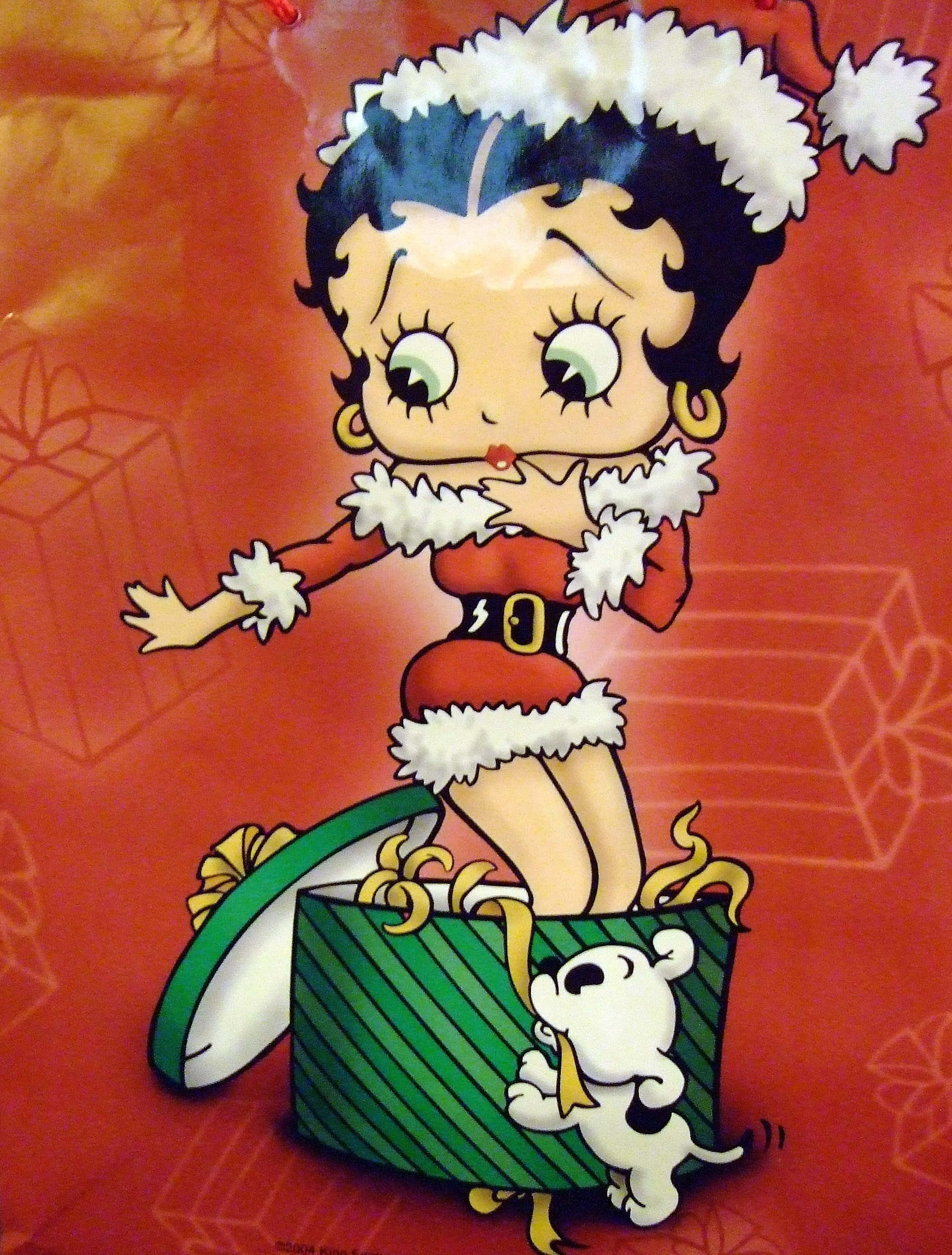 貝蒂娃娃 桌布 壁紙 — Betty Boop 穿著節日聖誕老人服裝，從綠色條紋禮物盒中出現，旁邊有一隻白色小狗，背景為紅色。