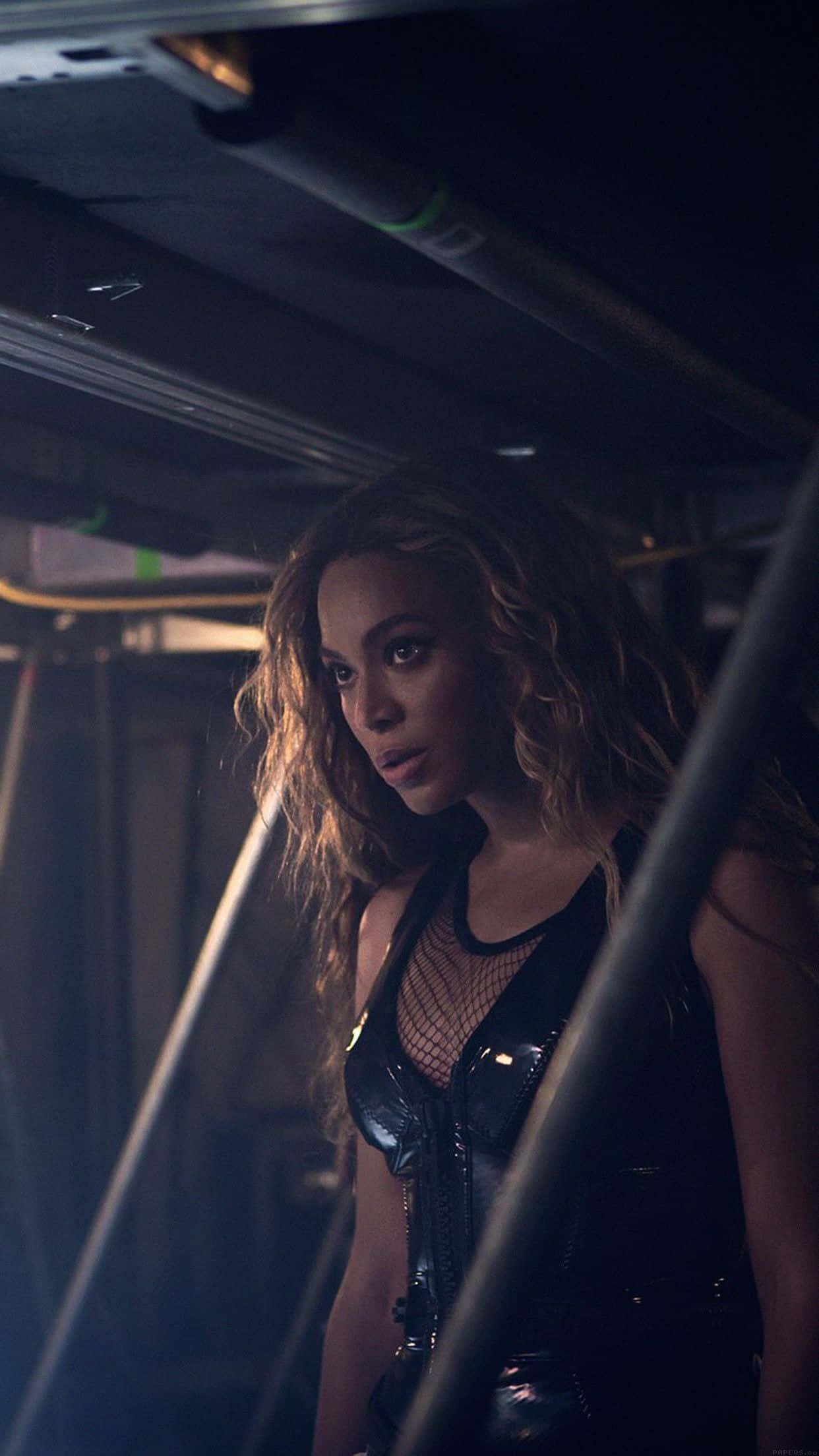 碧昂絲 桌布 壁紙 — Beyoncé 在一個由金屬條框住的昏暗工業空間中，強烈地凝視。