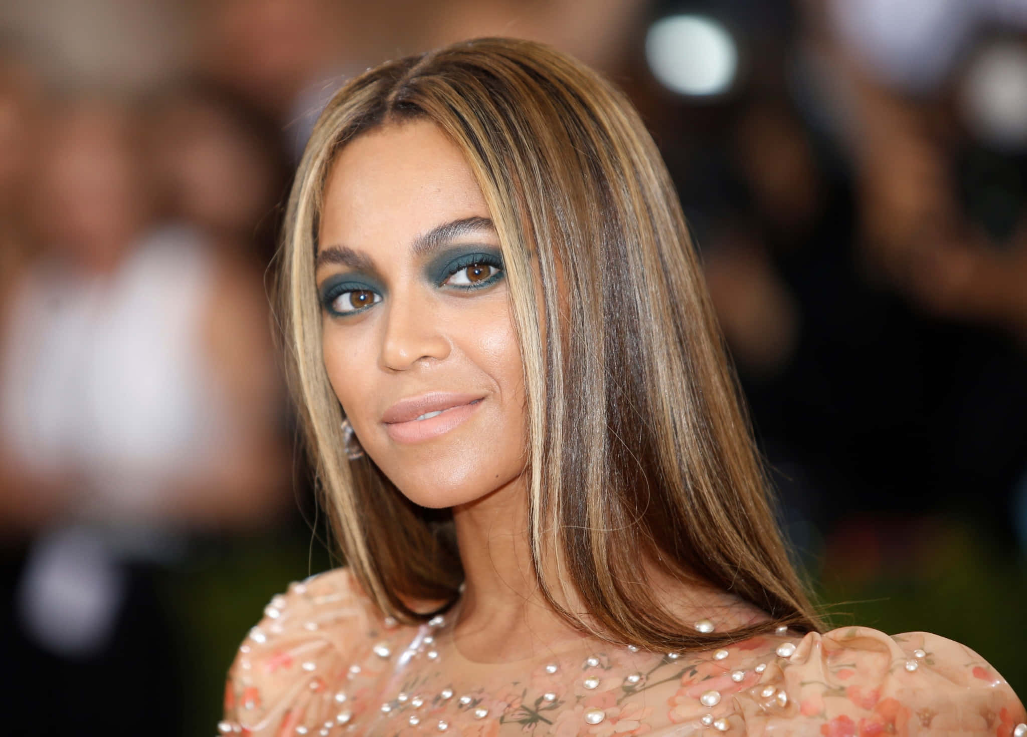 碧昂絲 桌布 壁紙 — Beyoncé 在一個華麗的活動中，穿著花卉珠飾長袍，搭配大膽的青綠色眼妝，溫柔地微笑。