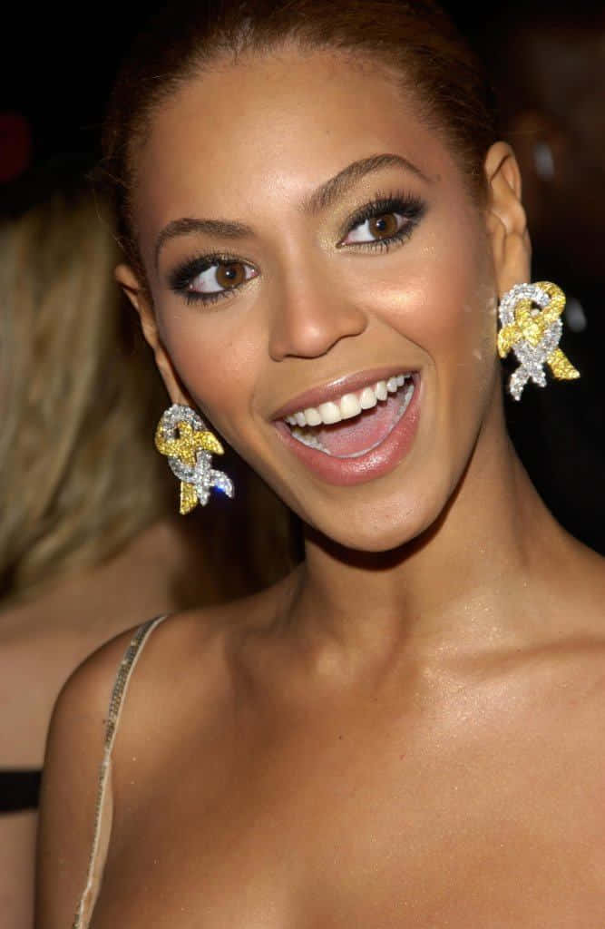 Smile 桌布 壁紙 — Beyoncé 在一個華麗的活動中戴著耀眼的金色和鑽石蝴蝶結耳環，燦爛地微笑。