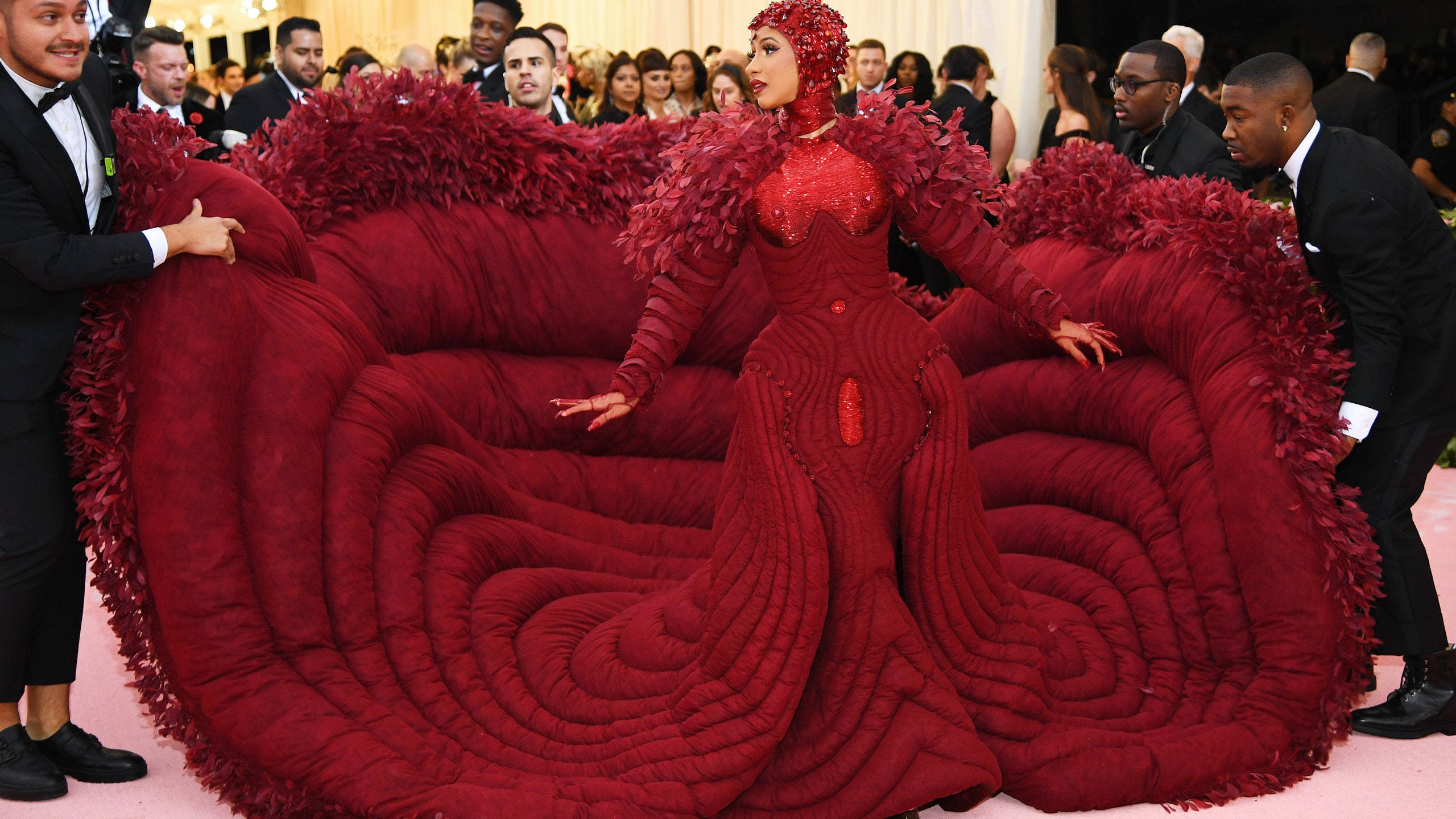 cardi 桌布 壁紙 — Beyoncé 在一個華麗的紅地毯活動中穿著一件戲劇性的紅色絎縫連衣裙，邊緣有羽毛裝飾。