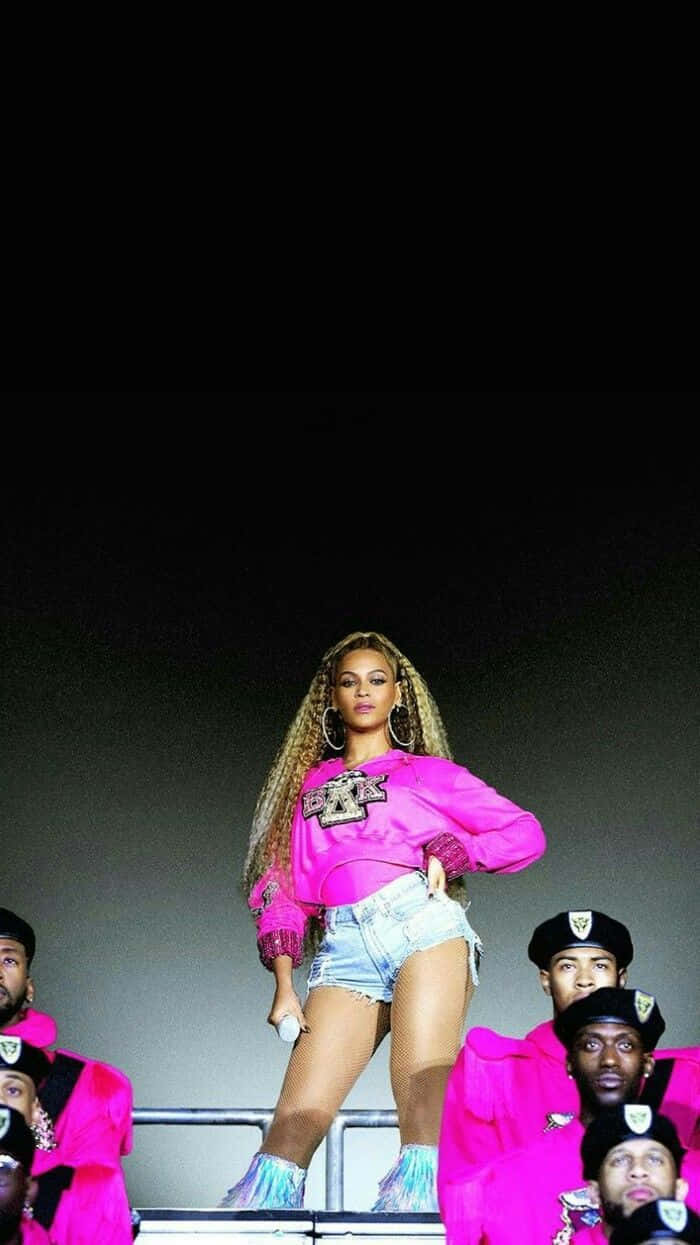 碧昂絲 桌布 壁紙 — Beyoncé 在明亮的演唱會燈光下，身穿鮮豔粉紅服裝，被身穿搭配服飾的舞者包圍，主宰舞台。