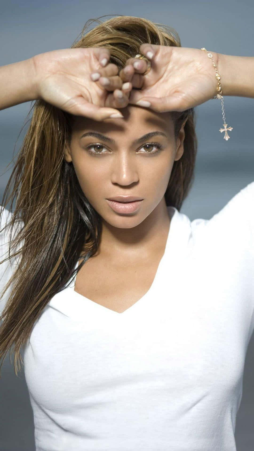 碧昂絲 桌布 壁紙 — Beyoncé 在柔和灰色背景前用手托住臉頰，身穿白色V領襯衫擺姿勢。