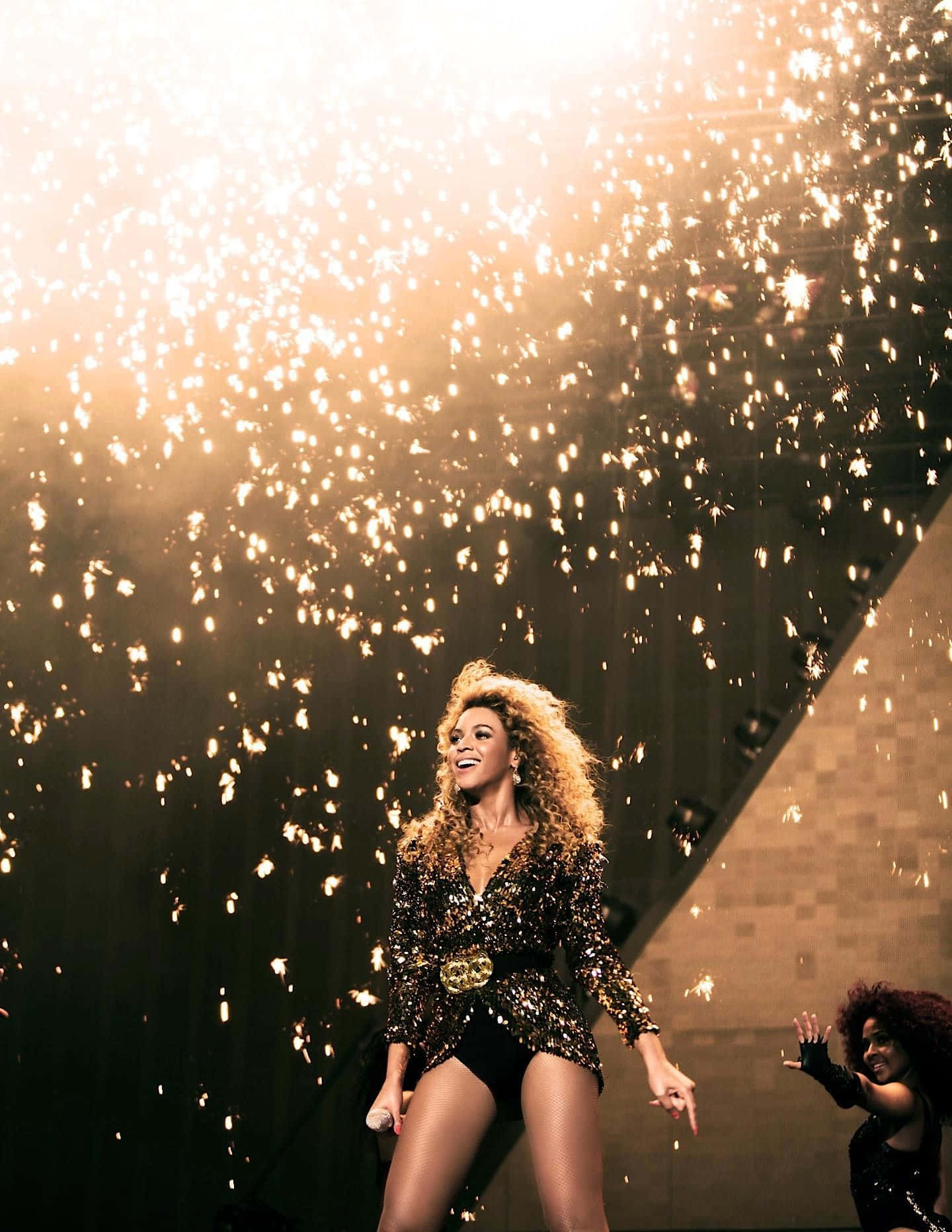 碧昂絲 桌布 壁紙 — Beyoncé 在舞台上散發喜悅，金色火花如瀑布般在她周圍灑落，構成一個耀眼的演唱會時刻。