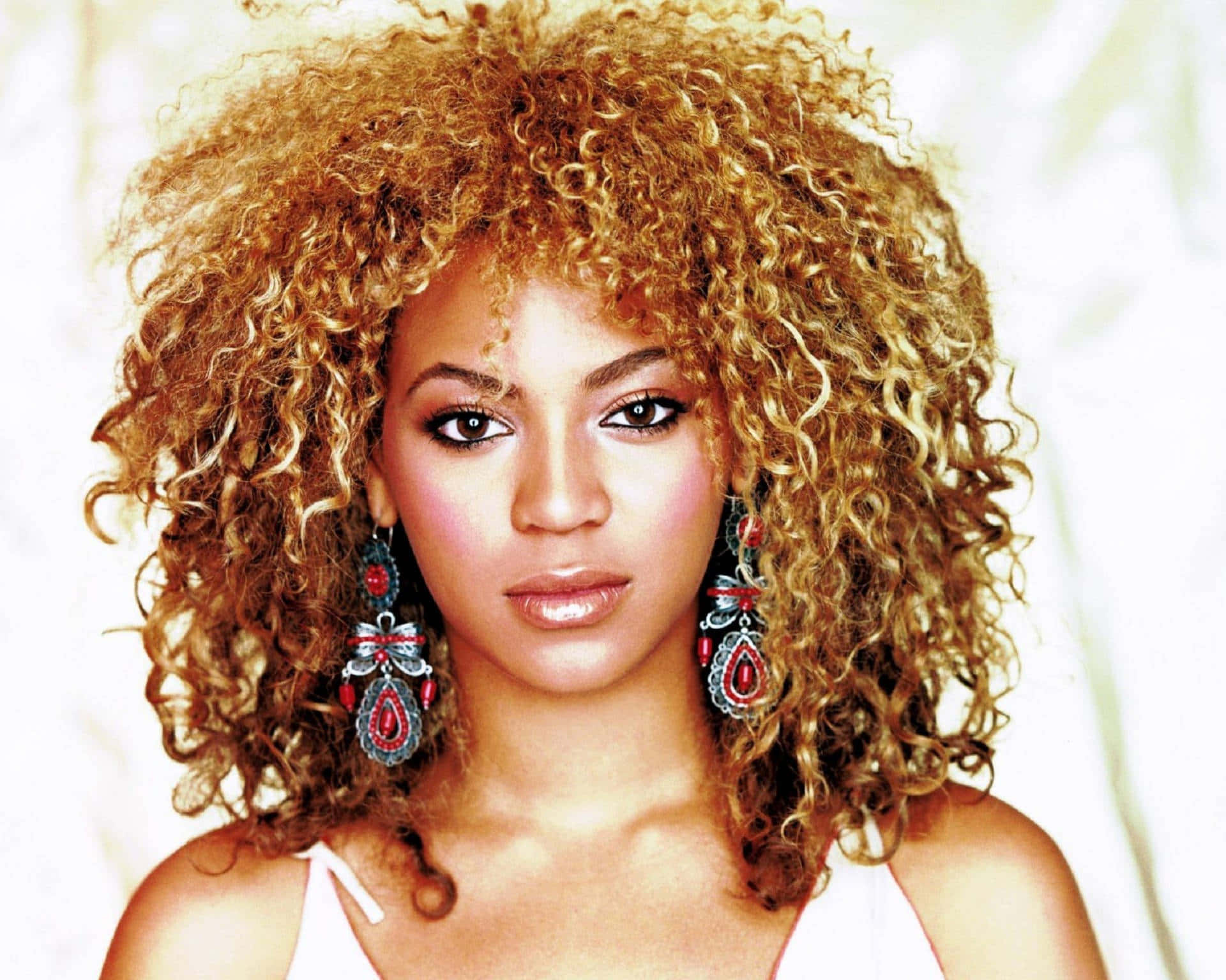 碧昂絲 桌布 壁紙 — Beyoncé 擁有豐盈金色捲髮和華麗紅色耳環，直視柔和的白色背景。
