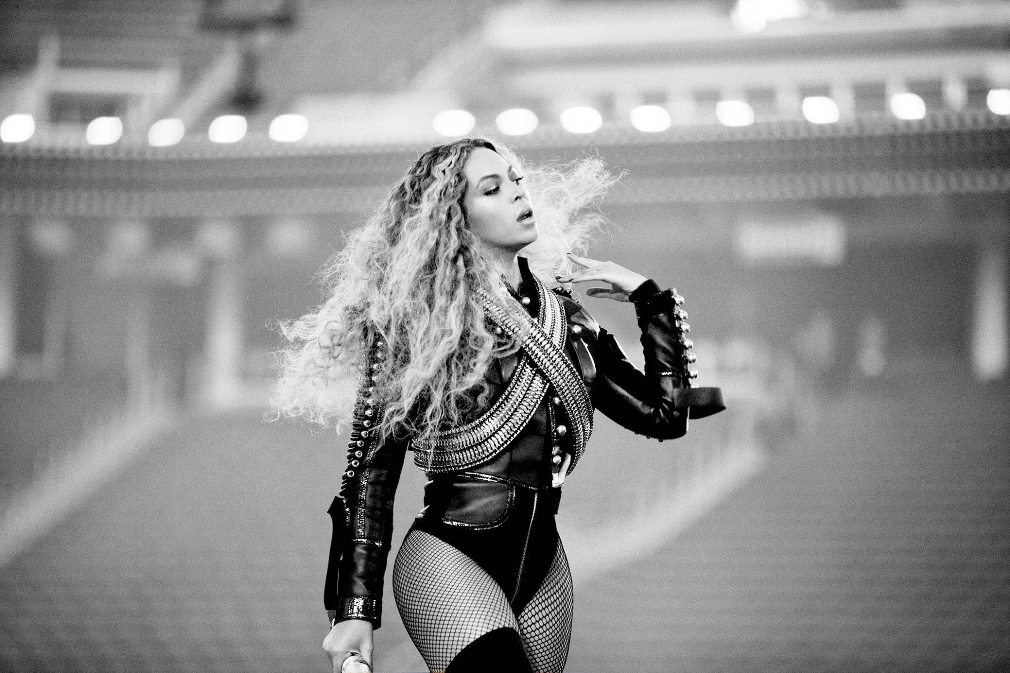 碧昂絲 桌布 壁紙 — Beyoncé 身穿鉚釘皮革服裝，秀髮飄逸，在戲劇性的黑白演唱會照片中主宰舞台。