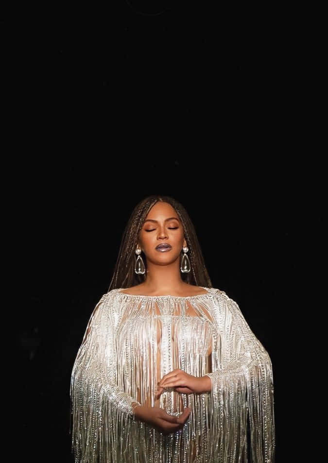 碧昂絲 桌布 壁紙 — Beyoncé 身穿閃閃發光的銀色流蘇長裙，在純黑背景前靜靜站立，閉上眼睛，陷入平靜的沉思。