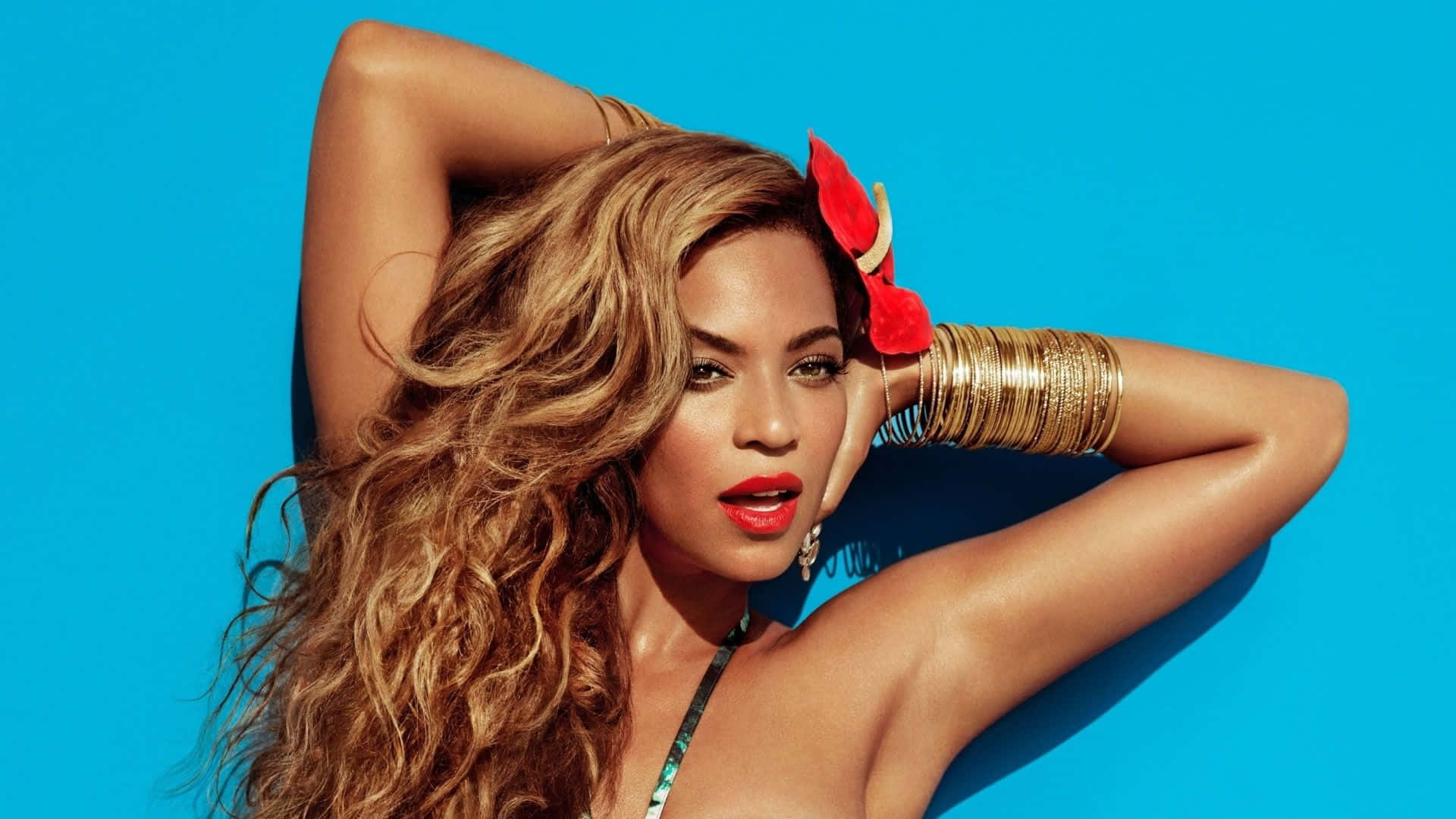 碧昂絲 桌布 壁紙 — Beyonce 在充滿活力的藍色背景前自信地擺姿勢，長長的波浪形頭髮和鮮豔的紅色唇膏。
