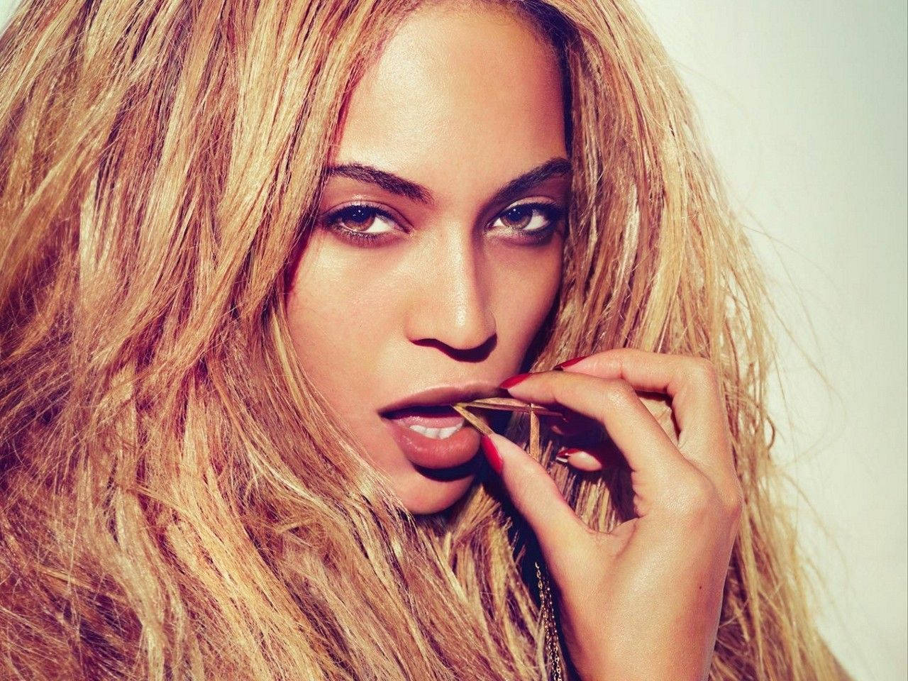 碧昂絲 桌布 壁紙 — Beyonce 金色頭髮和紅色指甲，在柔和背景下以強烈眼神塗口紅。