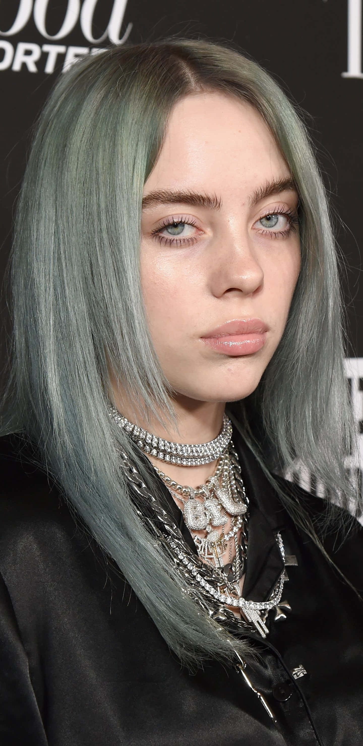 怪奇比莉 桌布 壁紙 — Billie Eilish 擁有淡綠色頭髮和層疊銀色項鍊，身穿黑色緞面上衣，直視鏡頭。