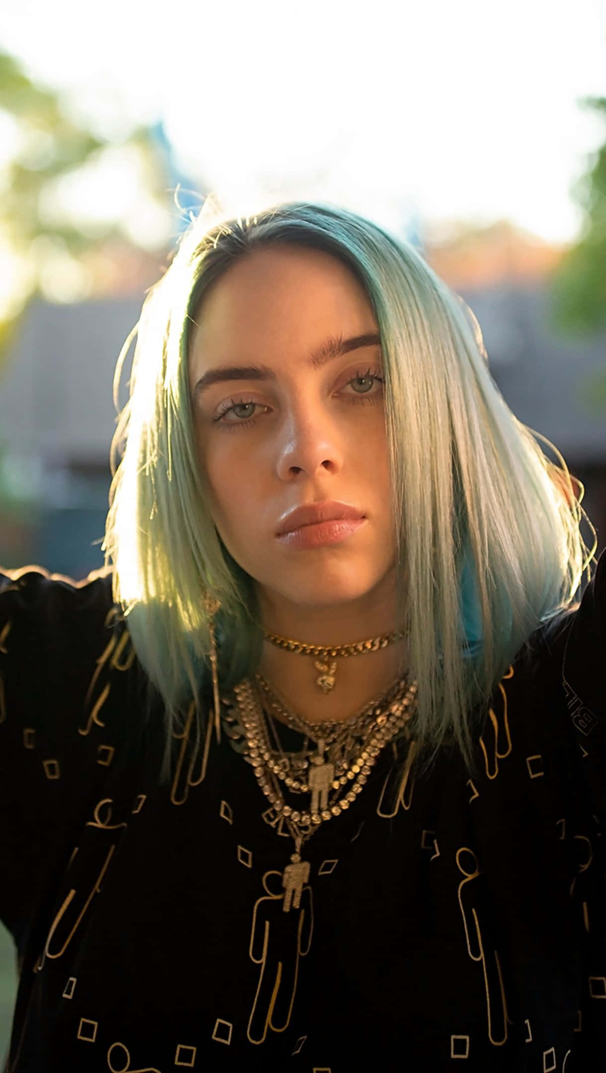 怪奇比莉 桌布 壁紙 — Billie Eilish 淺藍色頭髮和層疊金項鍊，在溫暖的金色陽光下直視鏡頭。