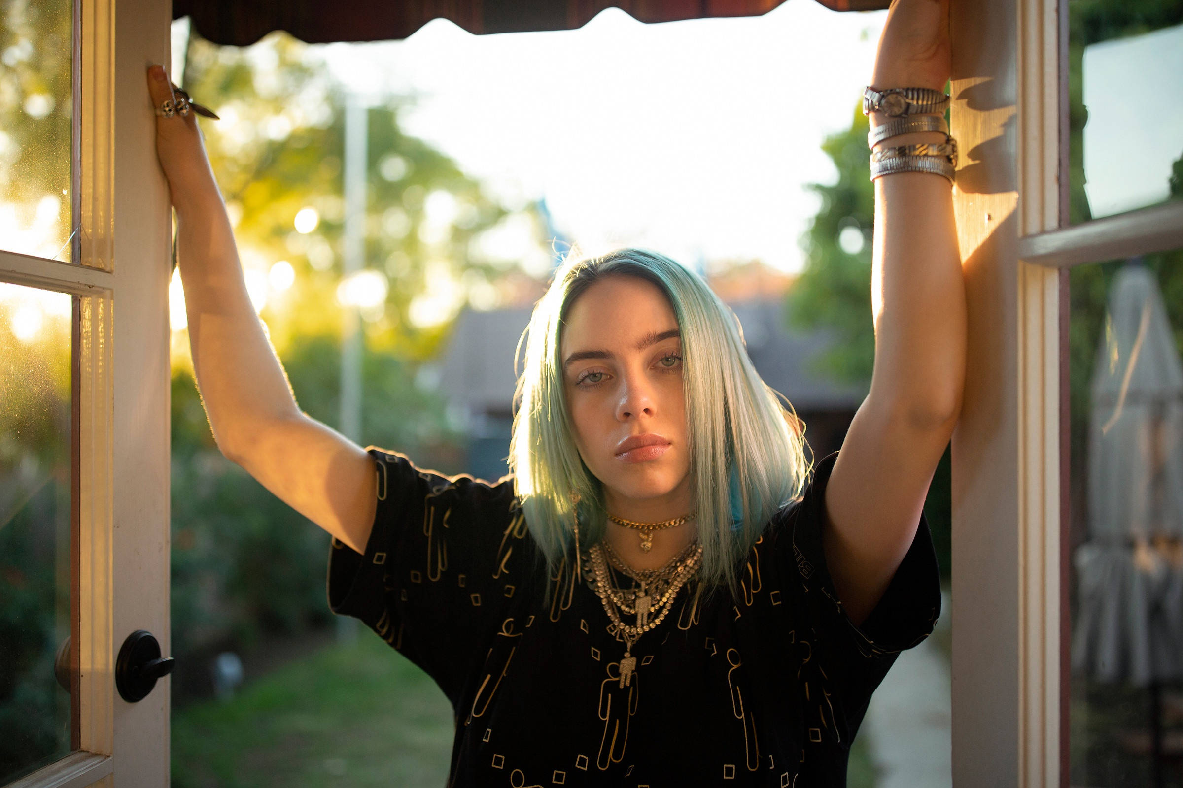 怪奇比莉 4K 桌布 壁紙 — Billie Eilish 舉起雙臂，靠在陽光普照的窗框上，她的藍色頭髮在金色午後光線中閃耀。