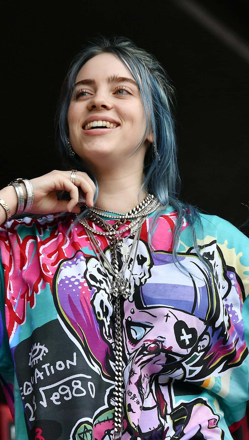 怪奇比莉 桌布 壁紙 — Billie Eilish 藍色頭髮搭配層疊項鍊，在深色背景下燦爛微笑。