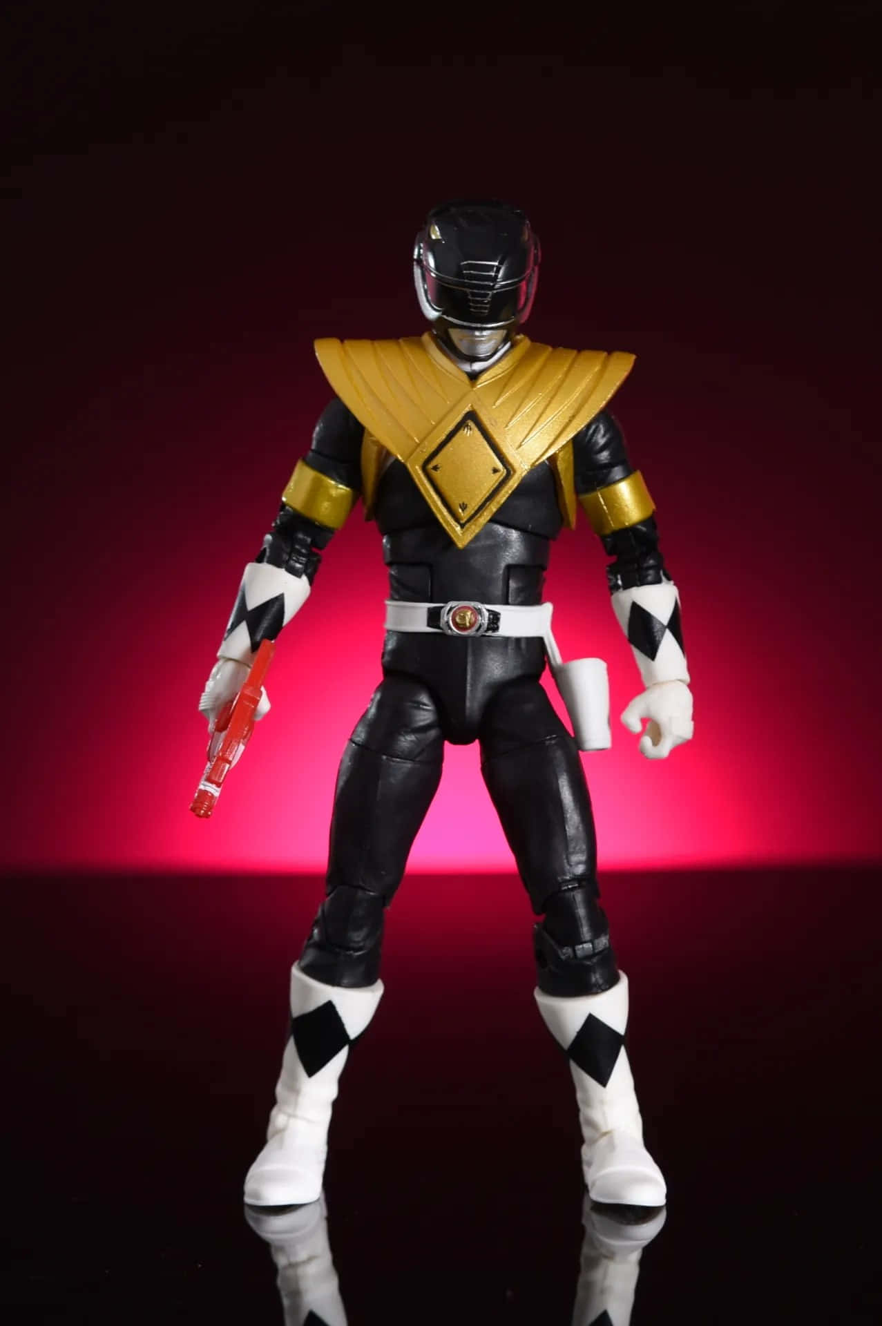  壁紙 — 一個黑色和金色的Power Ranger動作人偶在發光的紅色背景前擺出姿勢，地面有反射效果。