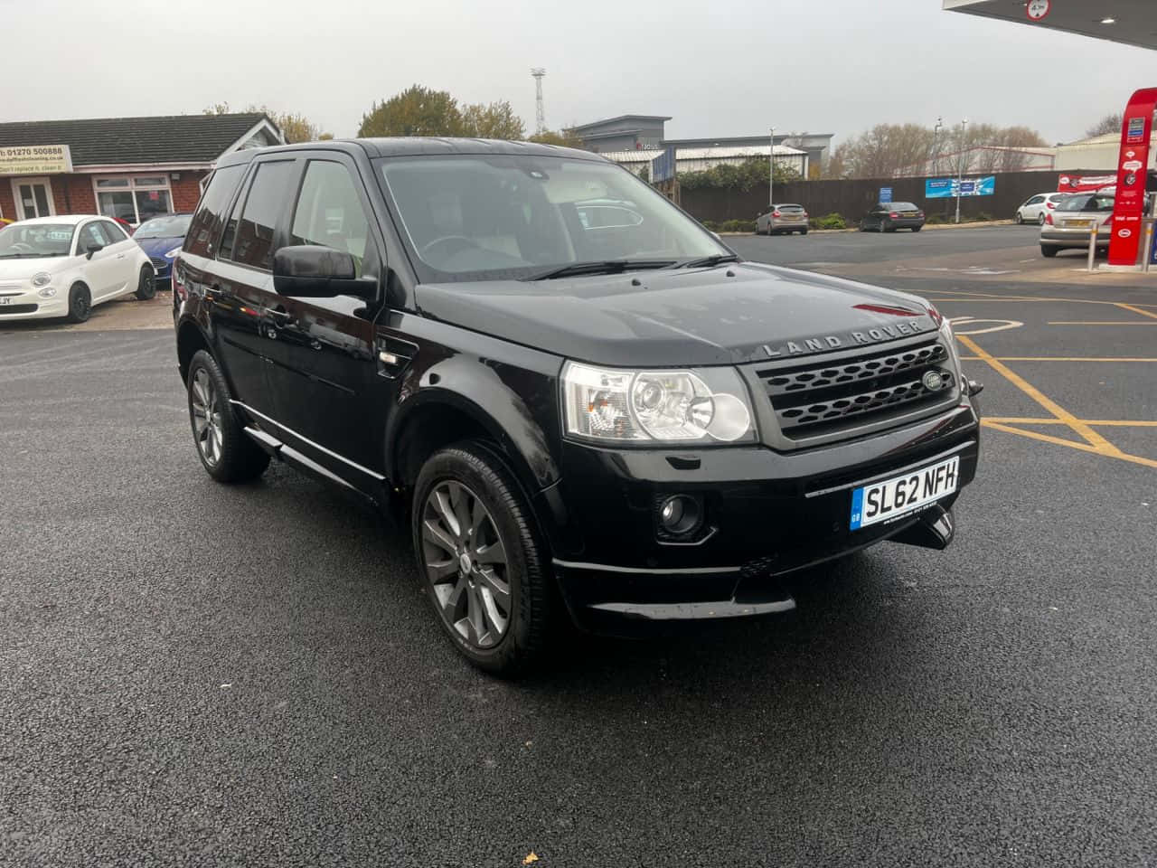 Land Rover Freelander 桌布 壁紙 — 一輛時尚的黑色Land Rover Freelander停放在加油站，陰天潮濕的路面反射著灰色的天空。