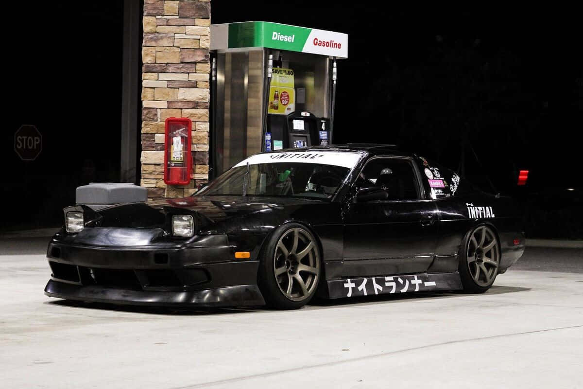  壁紙 — 一輛黑色改裝日產S13飄移車，帶有日文字和'INFIAL'品牌標誌，夜間在人工燈光下停泊在加油站。