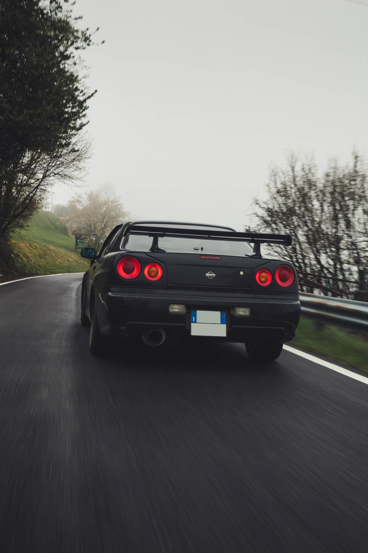 黑色跑車帶紅色尾燈在霧氣瀰漫的山路上行駛。 — 日產 Skyline GTR R34 壁紙