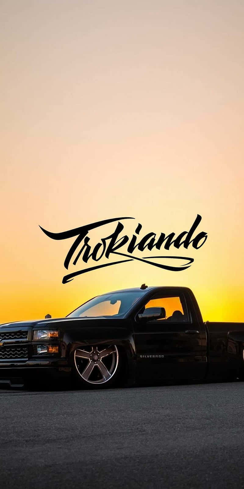  壁紙 — 一輛黑色皮卡車停在柏油路上，夕陽西下，天空呈現橙色光芒，並帶有「Trokiano」文字疊加。