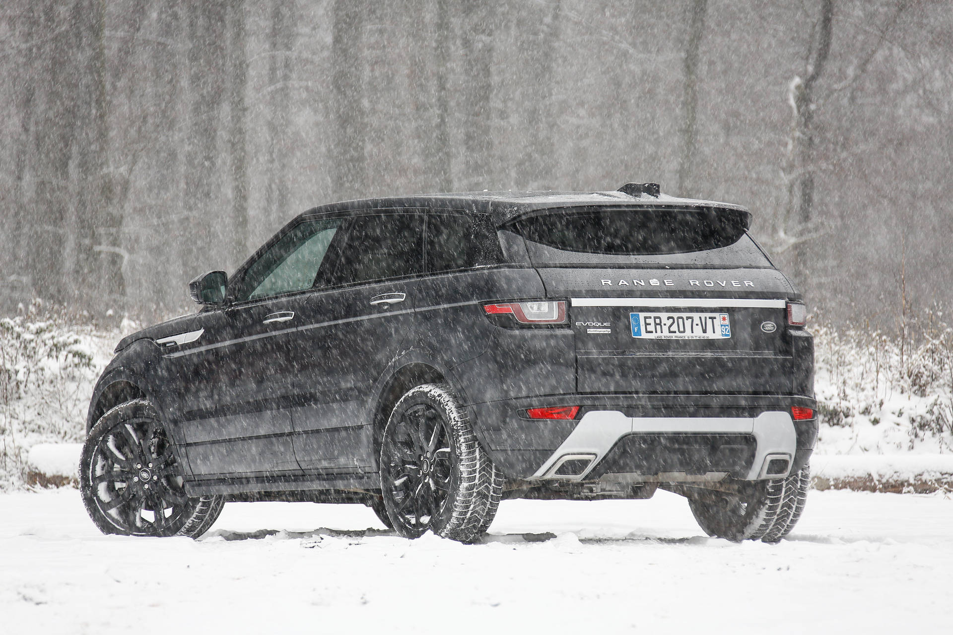 黑色 Range Rover Evoque 在冬季暴風雪中行駛於積雪森林。 — 4K 壁紙