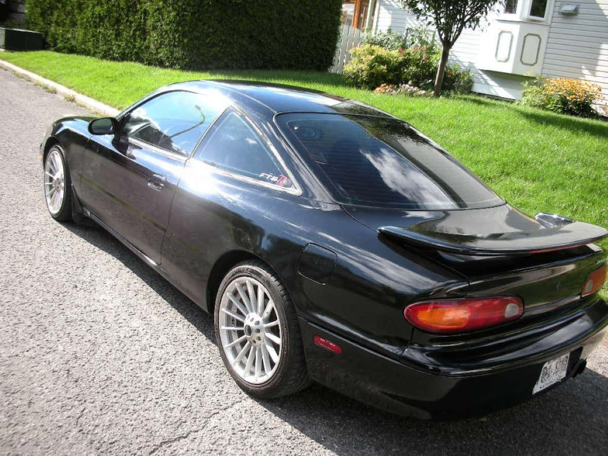 Mazda Mx-6 桌布 壁紙 — 一輛時尚的黑色跑車配銀色輪圈，停泊在住宅街道旁，旁邊有綠色草坪和白色房屋。