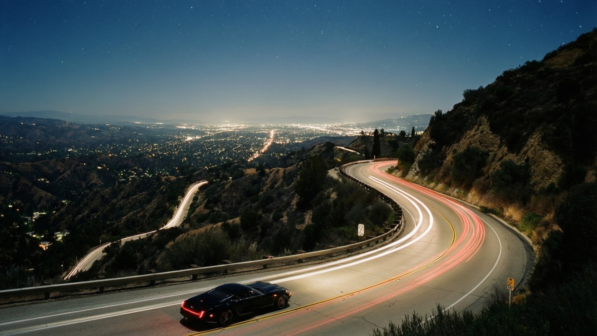 Mulholland Drive Night Curve 壁紙 — 一輛黑色跑車在蜿蜒的山路上行駛，下方是城市燈光，上方是繁星點點的夜空。