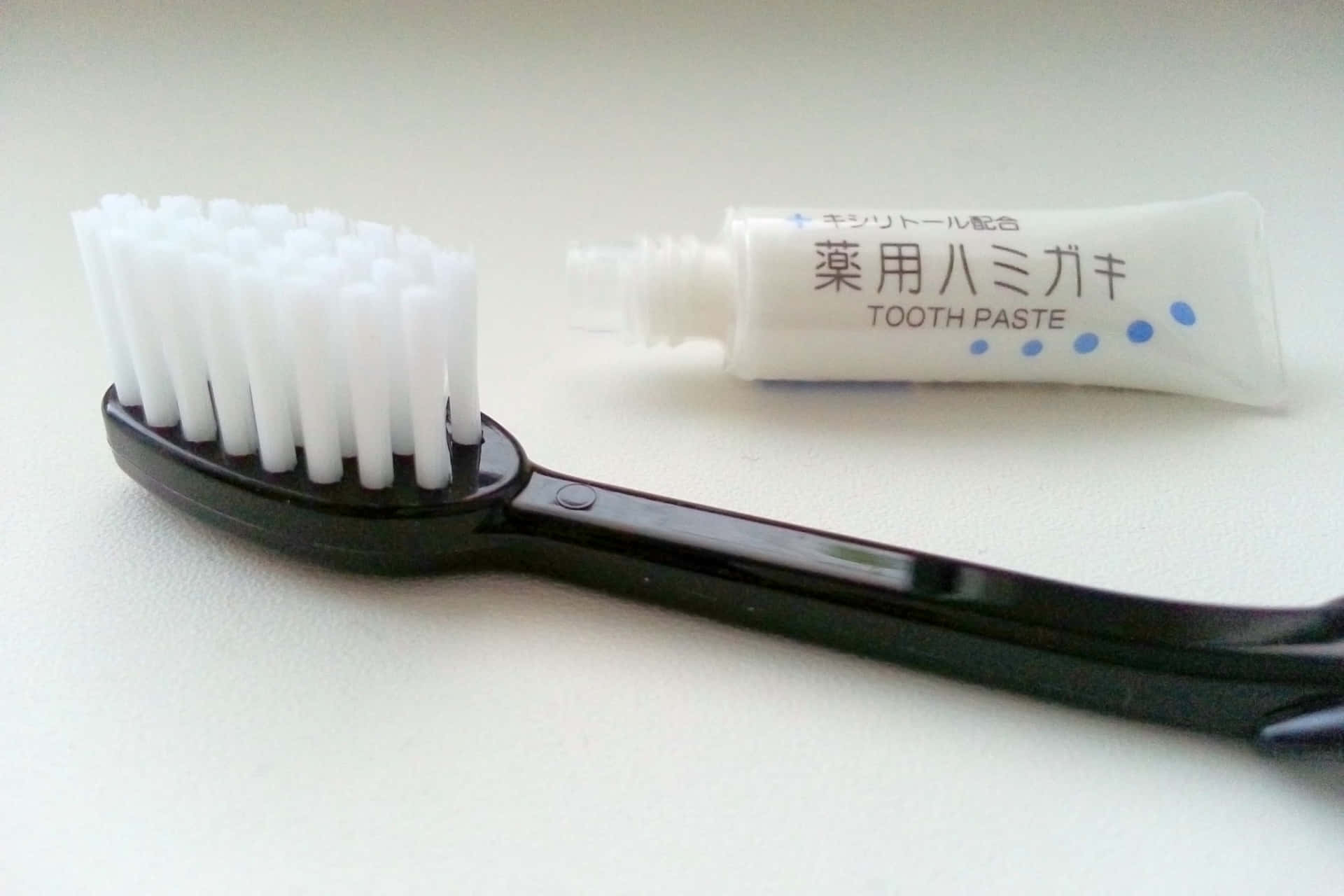 壁紙 — 一支黑色刷毛的牙刷放在白色平面上，旁邊是一條日本藥用牙膏。