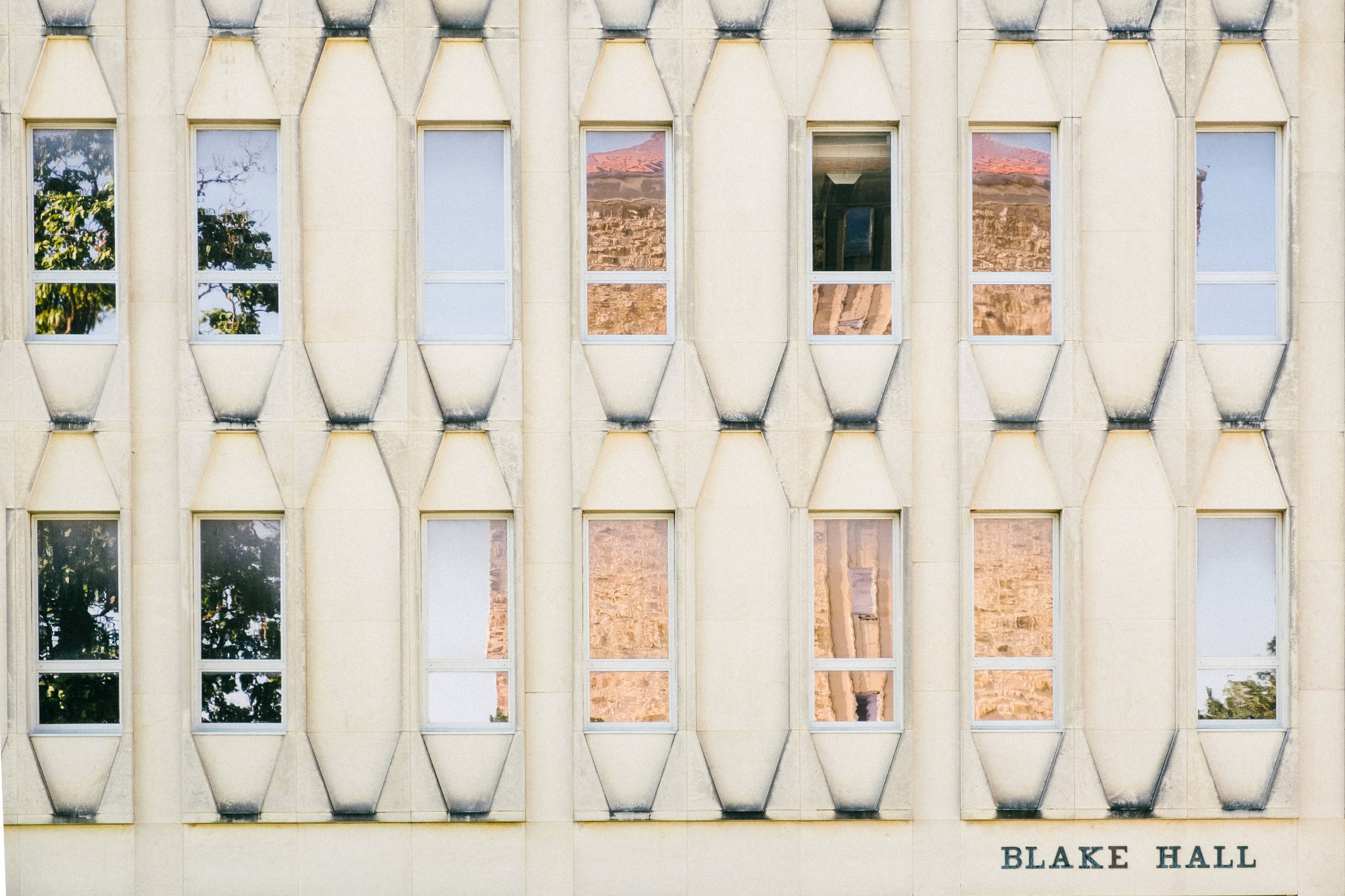 建築 桌布 壁紙 — Blake Hall 的幾何立面，窗戶映照出樹木和沙漠景觀，色調溫暖。