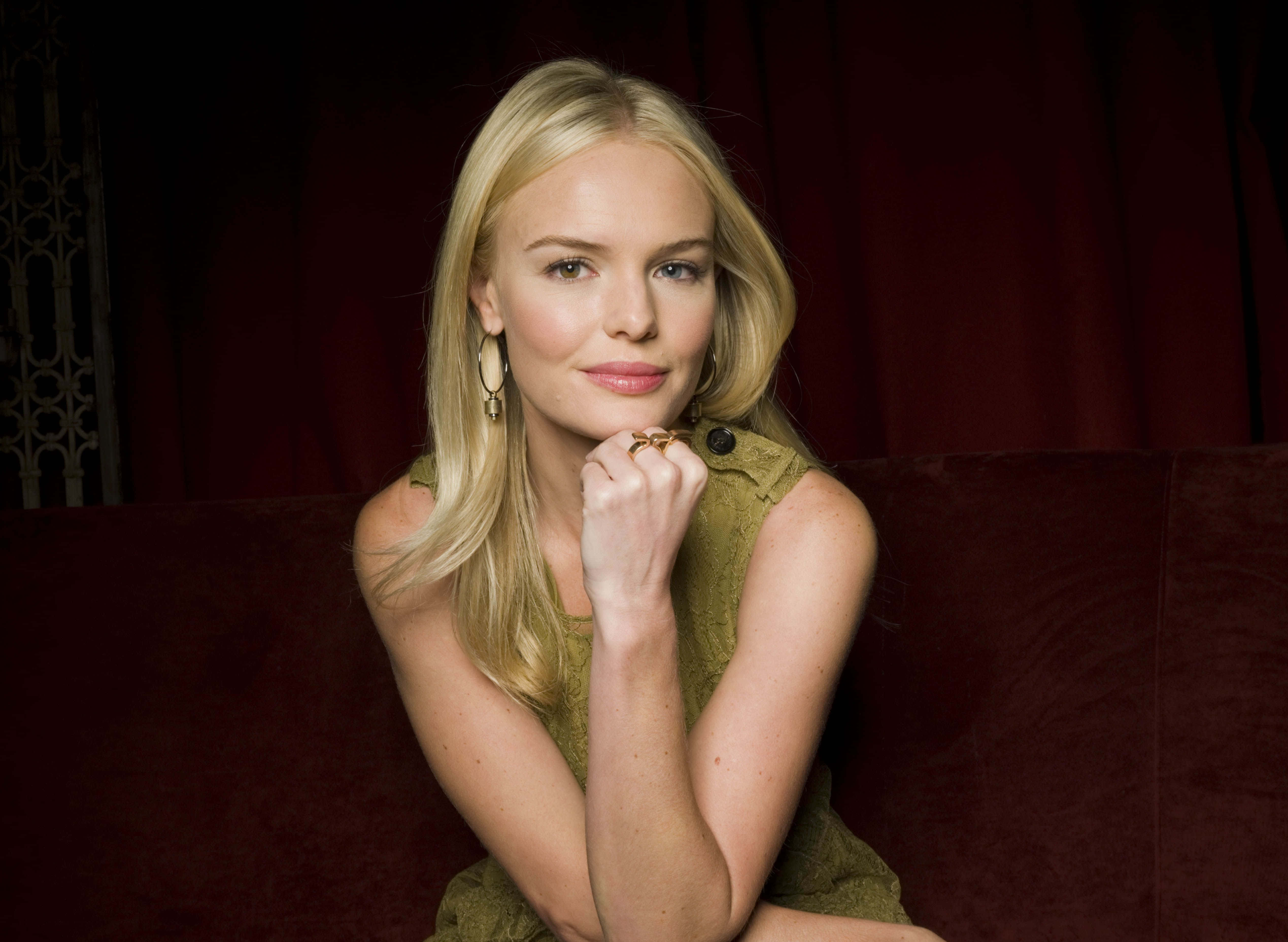 Kate Bosworth 桌布 壁紙 — 一位金髮女子穿著綠色連衣裙，在深色窗簾背景下若有所思地坐在一張豪華的紅色沙發上。