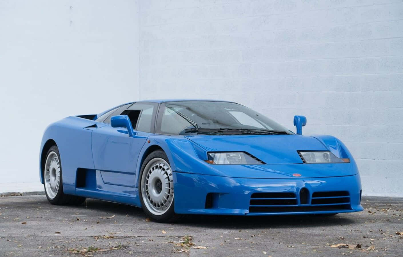 Bugatti Eb110 桌布 壁紙 — 一輛充滿活力的藍色Bugatti EB110超級跑車停放在灰色路面上的純白磚牆前。