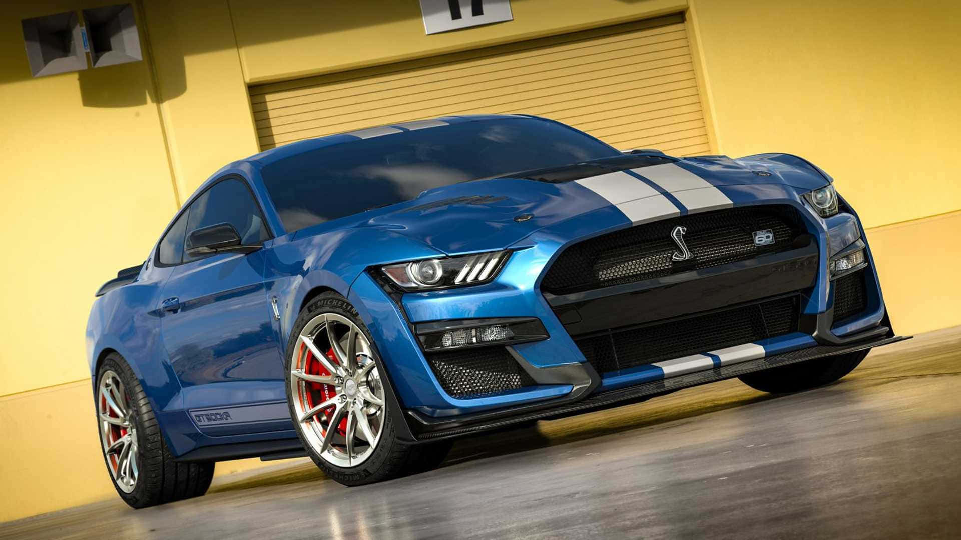  壁紙 — 一輛充滿活力的藍色福特野馬Shelby GT500，帶有白色賽車條紋和紅色制動卡鉗，停在車庫中。