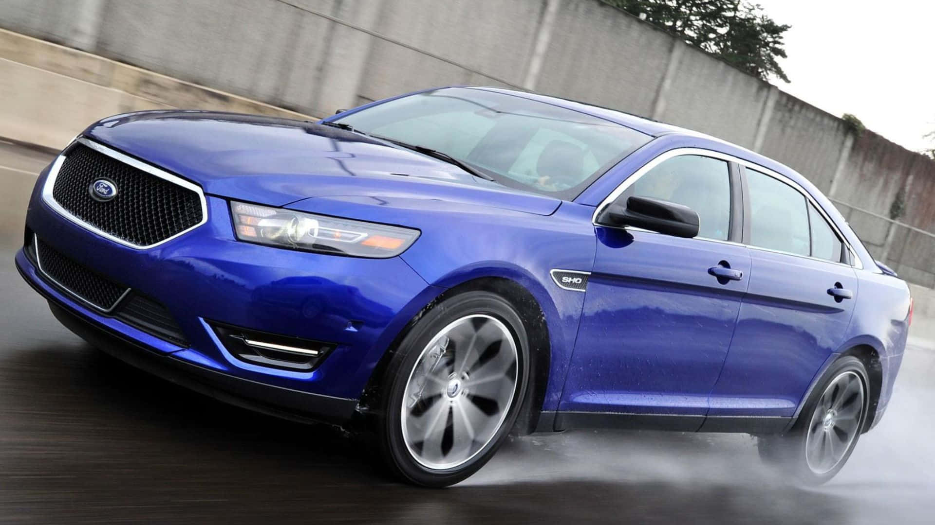Ford Taurus 桌布 壁紙 — 一輛充滿活力的藍色福特 Taurus SHO 轎車在潮濕的道路上奔馳，帶有動態模糊和輪胎水花。
