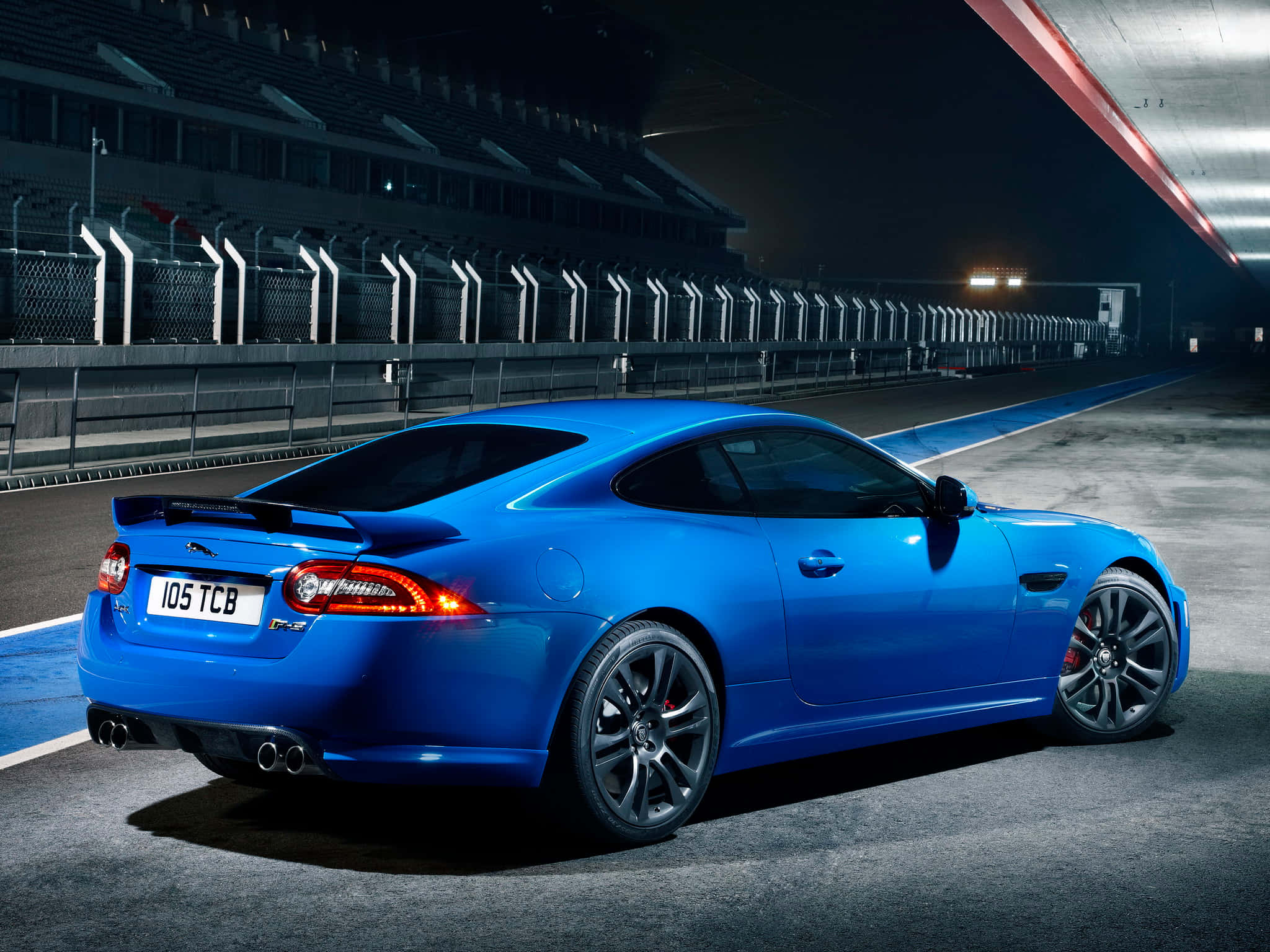 Jaguar Xkr 桌布 壁紙 — 一輛充滿活力的藍色積架跑車在夜間黑暗賽道的燈光下閃閃發光。