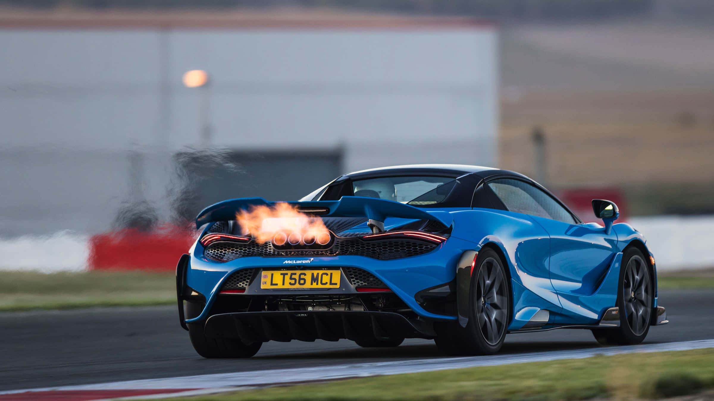 Mclaren 765lt 桌布 壁紙 — 一輛充滿活力的藍色McLaren跑車在賽道上飛馳，排氣管噴出火焰。