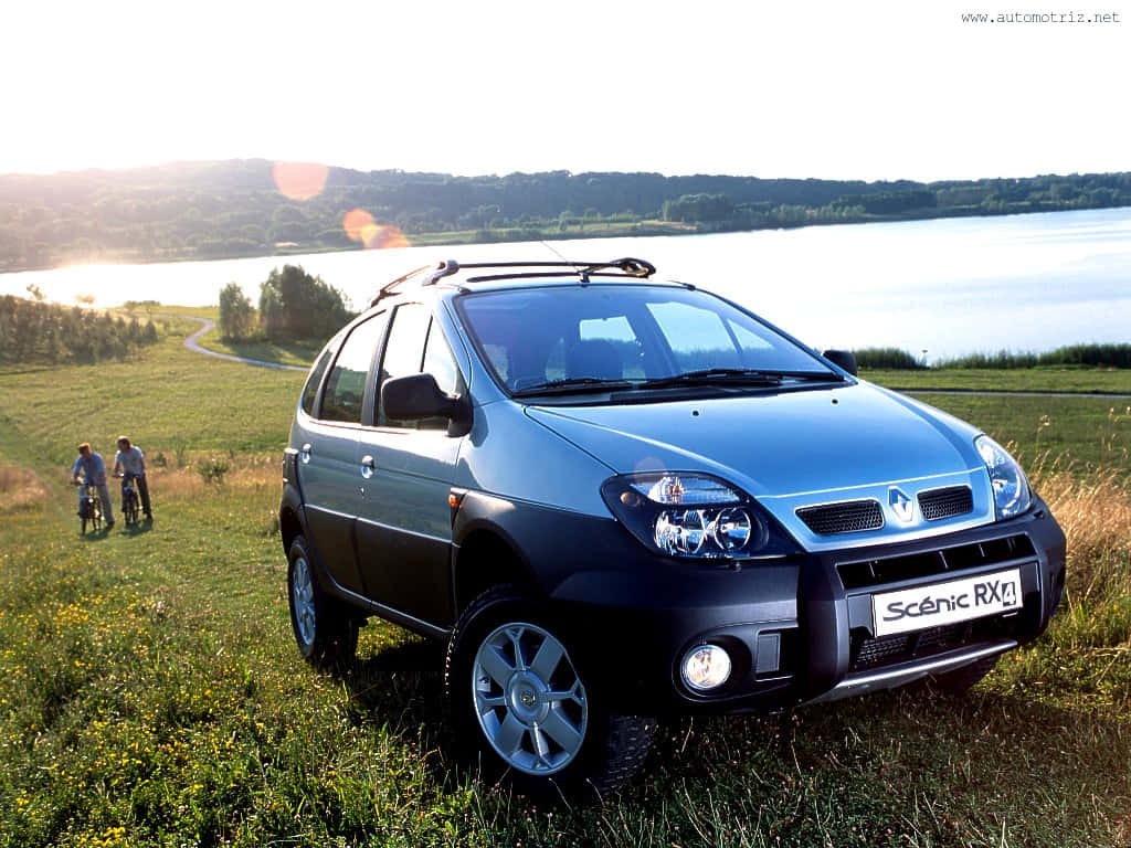 Renault Scenic 桌布 壁紙 — 一輛藍色雷諾 Scenic RX4 SUV 停在湖邊草地上，背景有兩位騎自行車的人，在溫暖的日落光線下。