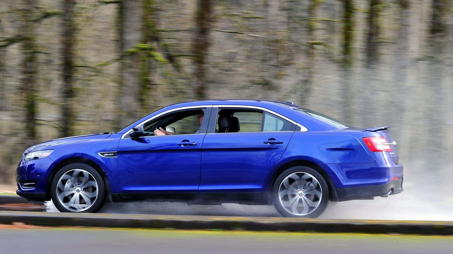 Ford Taurus 桌布 壁紙 — 一輛充滿活力的藍色轎車在道路上疾馳，模糊的森林背景營造出動態模糊效果。
